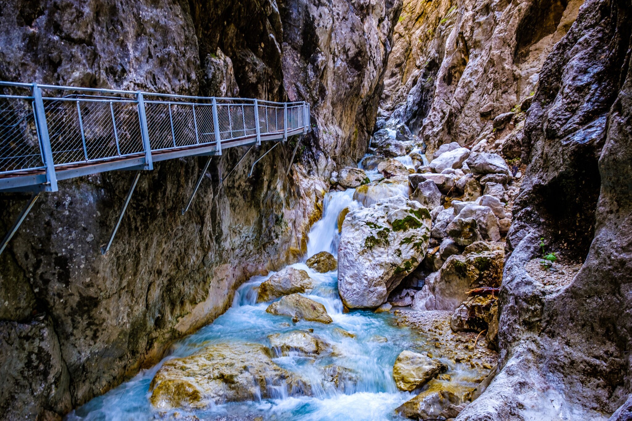 Enge Schlucht mit einem kleinen Wasserfall und einer schmalen Brücke an einer Felswand.