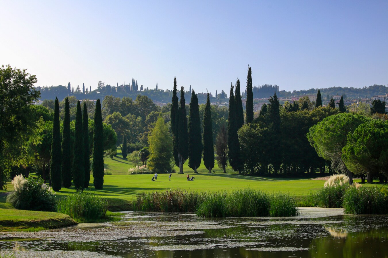 Ein kleiner See mit Blick auf eine Golfbahn und zwei Golfspieler:innen