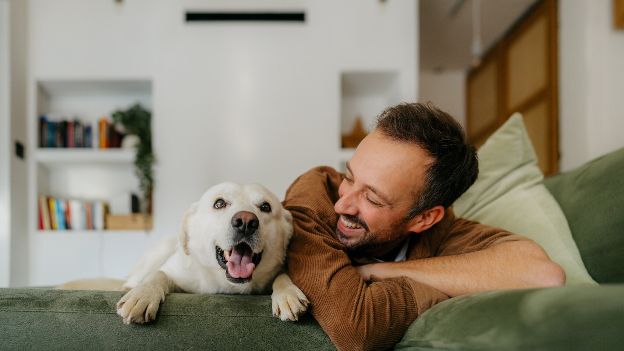 in lachender Mann und ein Hund liegen nebeneinander auf einem Sofa.