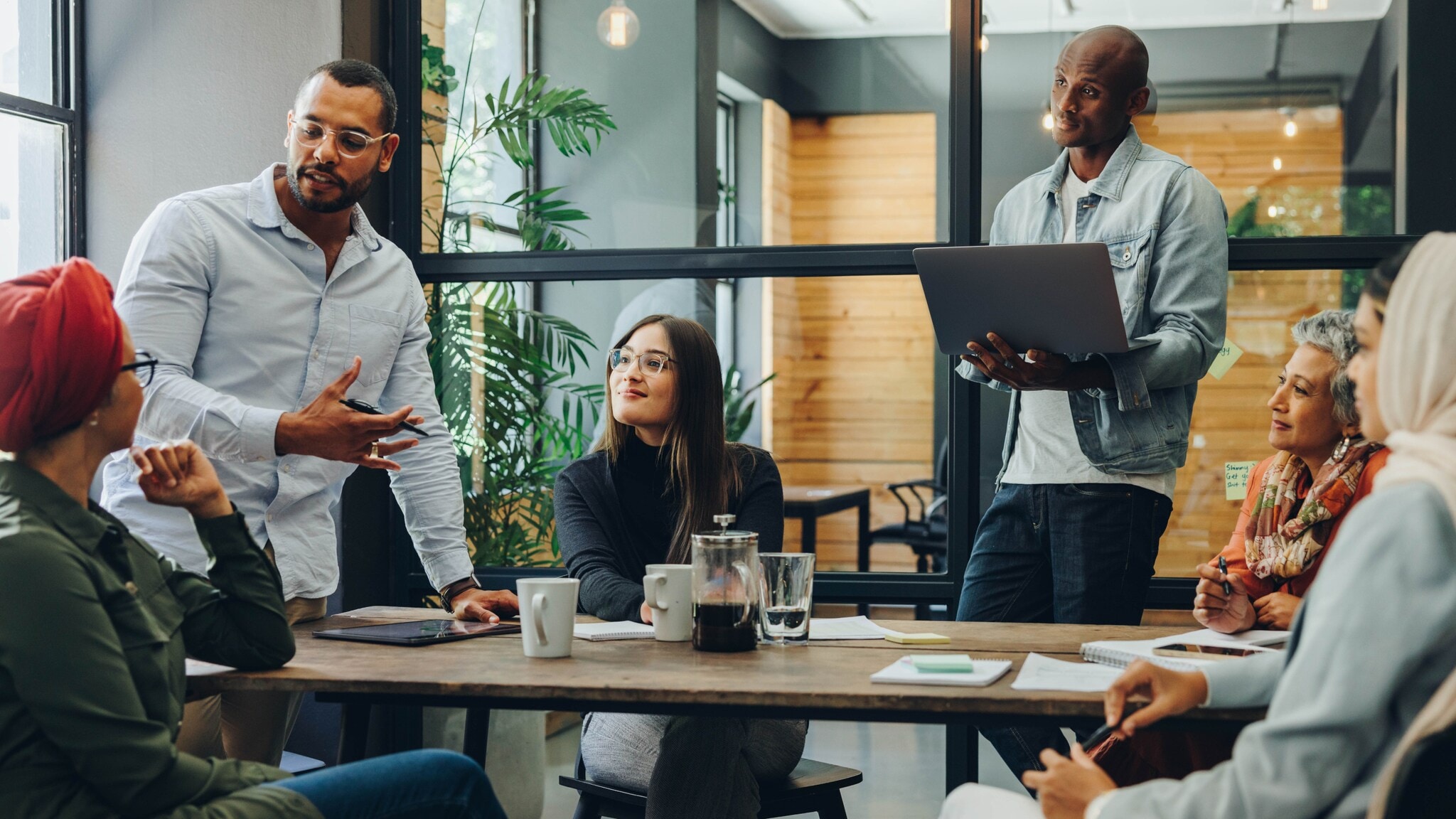 Mehrere Personen sitzen oder stehen an einem Tisch und schauen eine Person an, die spricht. Mehrere Personen sitzen oder stehen an einem Tisch und schauen eine Person an, die spricht.
