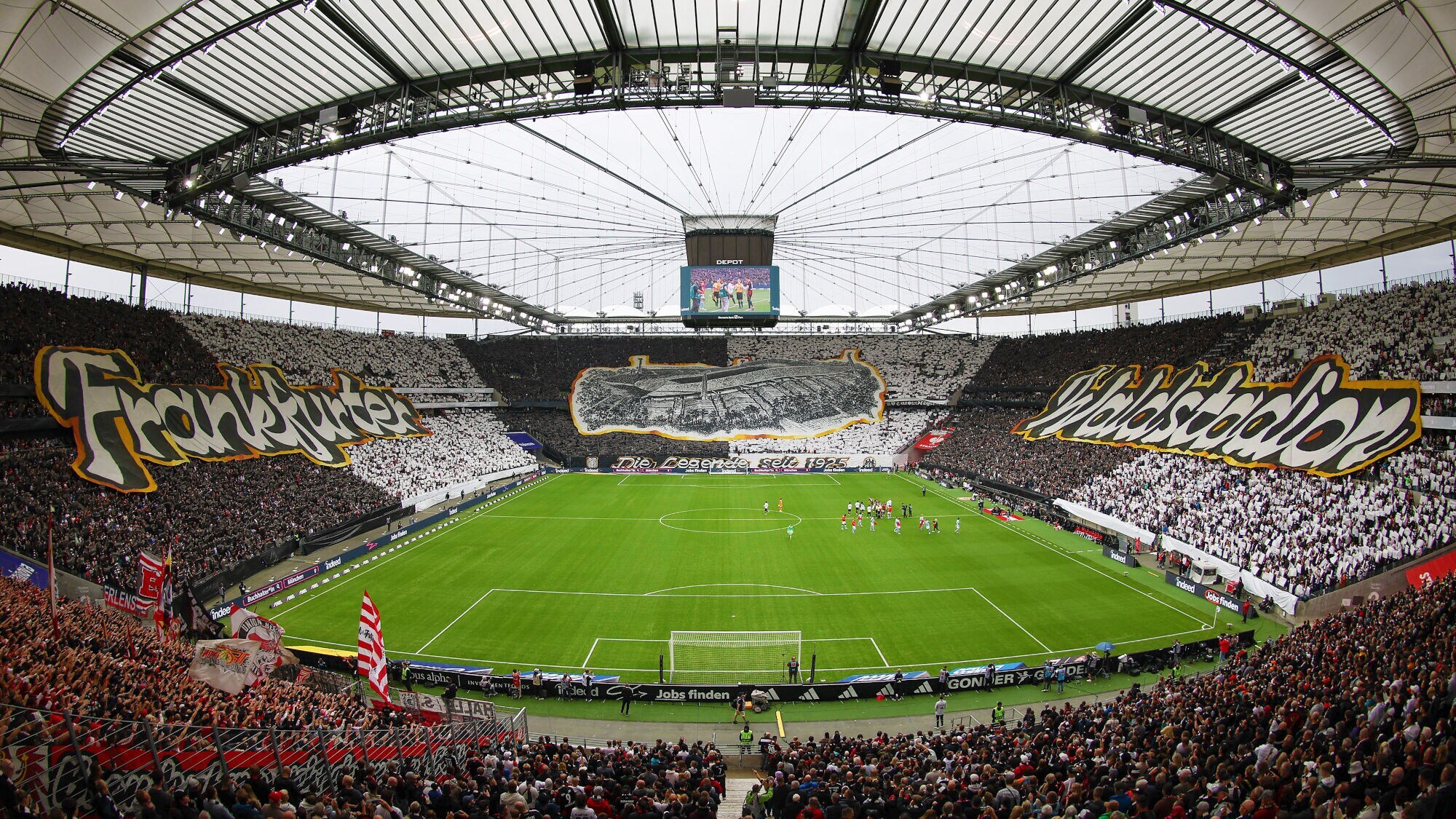 Fußballstadion mit gefüllten Zuschauerplätzen und großen Stoffbanner mit Aufdrucken