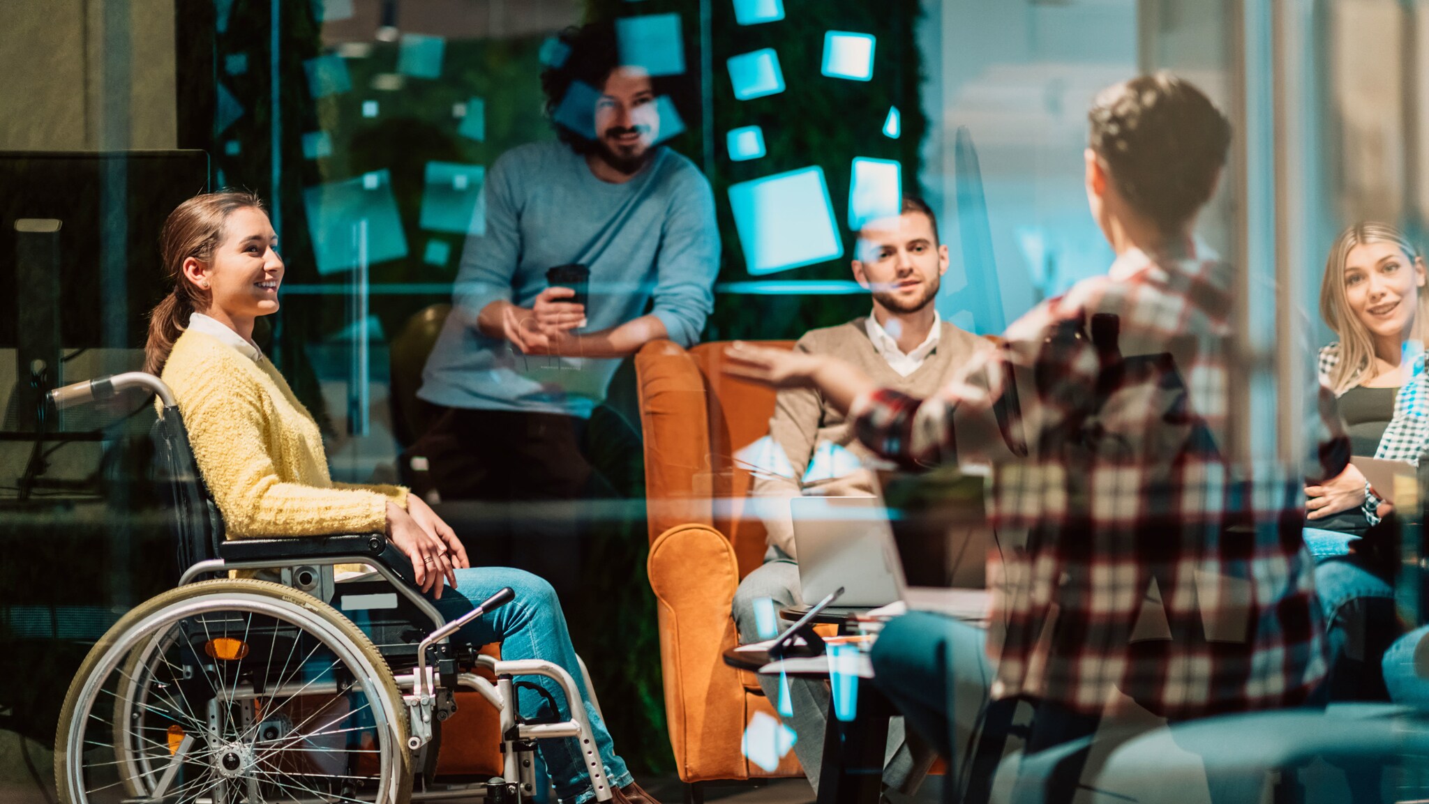 Eine Frau im Rollstuhl und weitere Personen reden in einem Raum mit Glaswand.