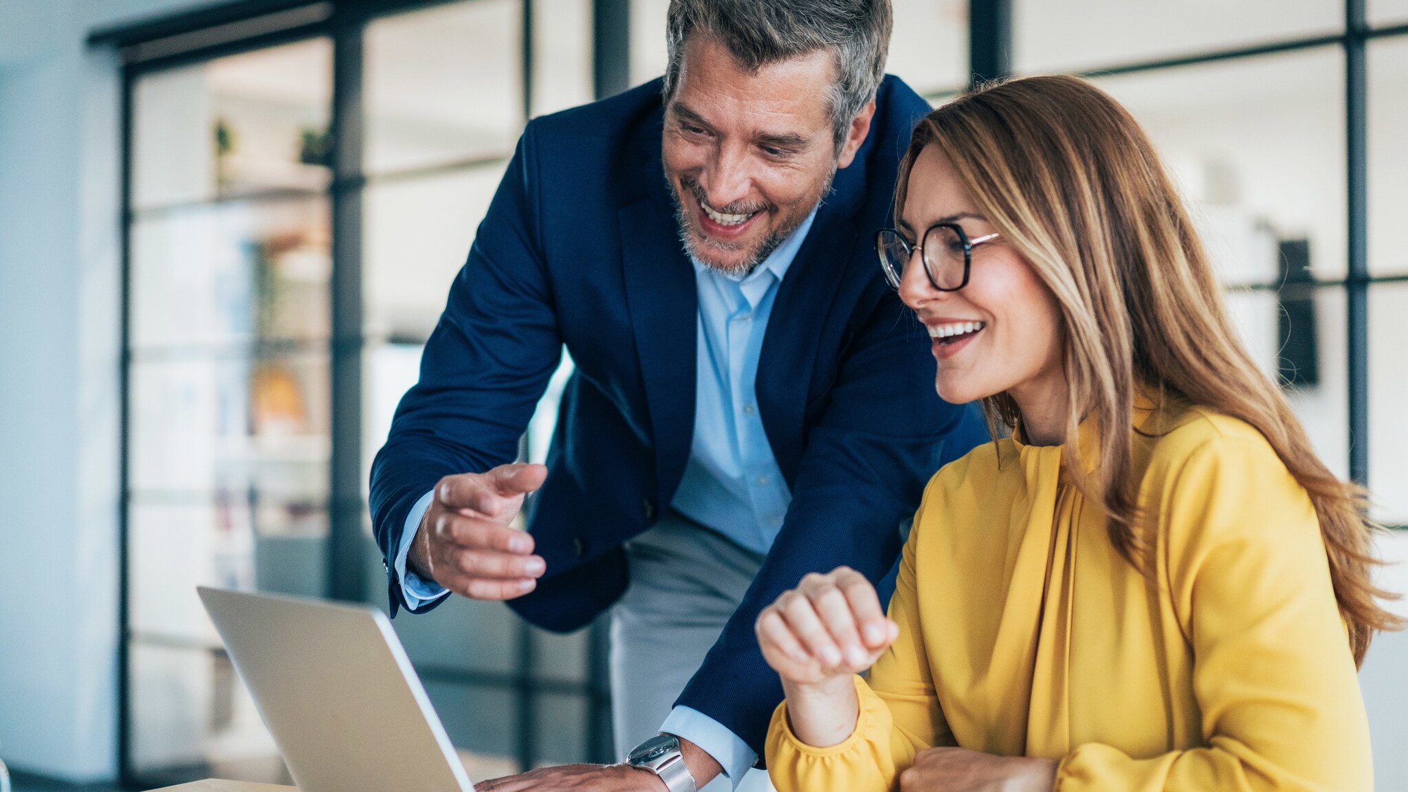 Eine Frau und ein Mann in Business-Kleidung schauen lächelnd zusammen auf einen Laptop. Eine Frau und ein Mann in Business-Kleidung schauen lächelnd zusammen auf einen Laptop.