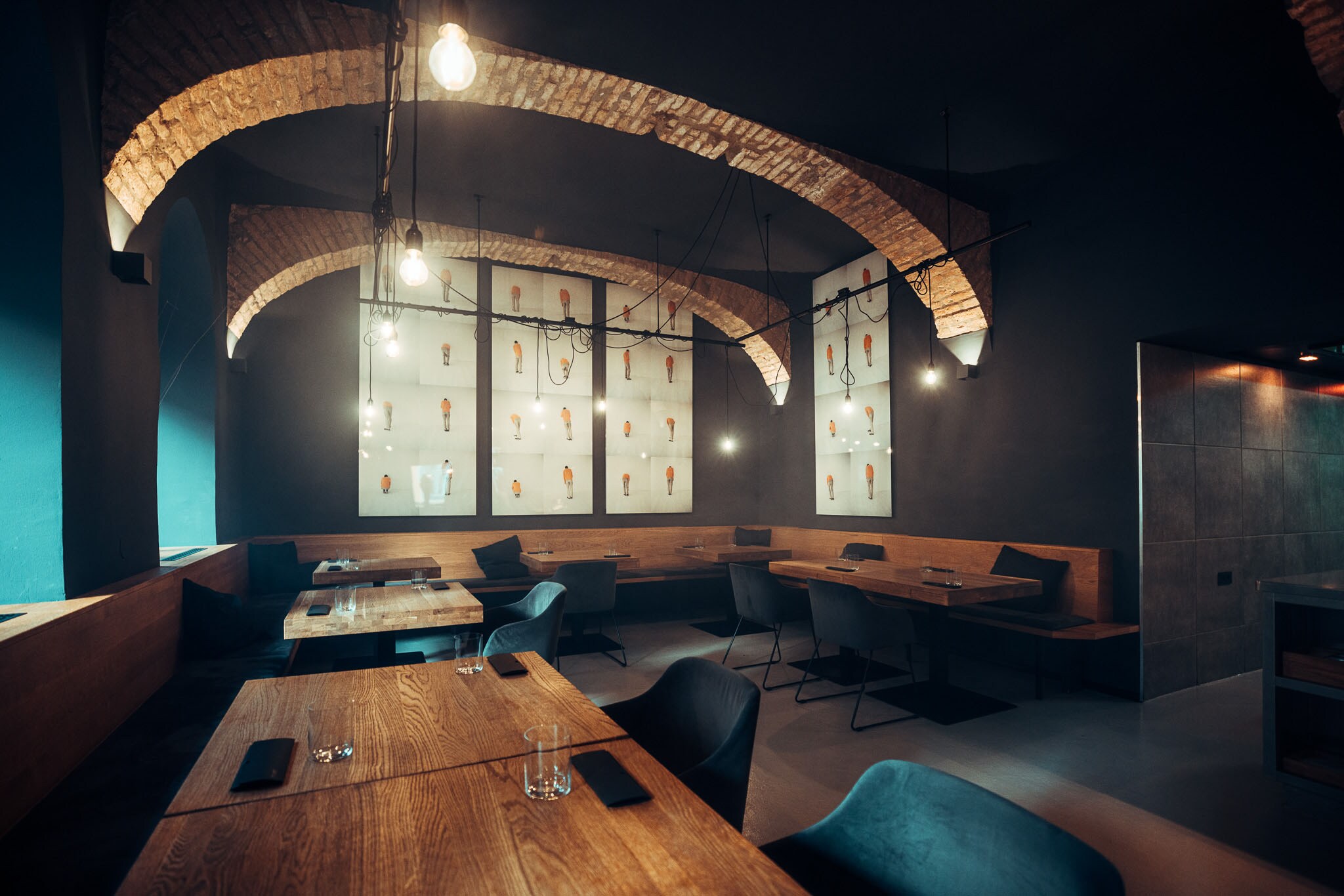 Moderner Speisesaal mit eingedeckten Holztischen und dunklen Wänden mit Gewölbedecke.
