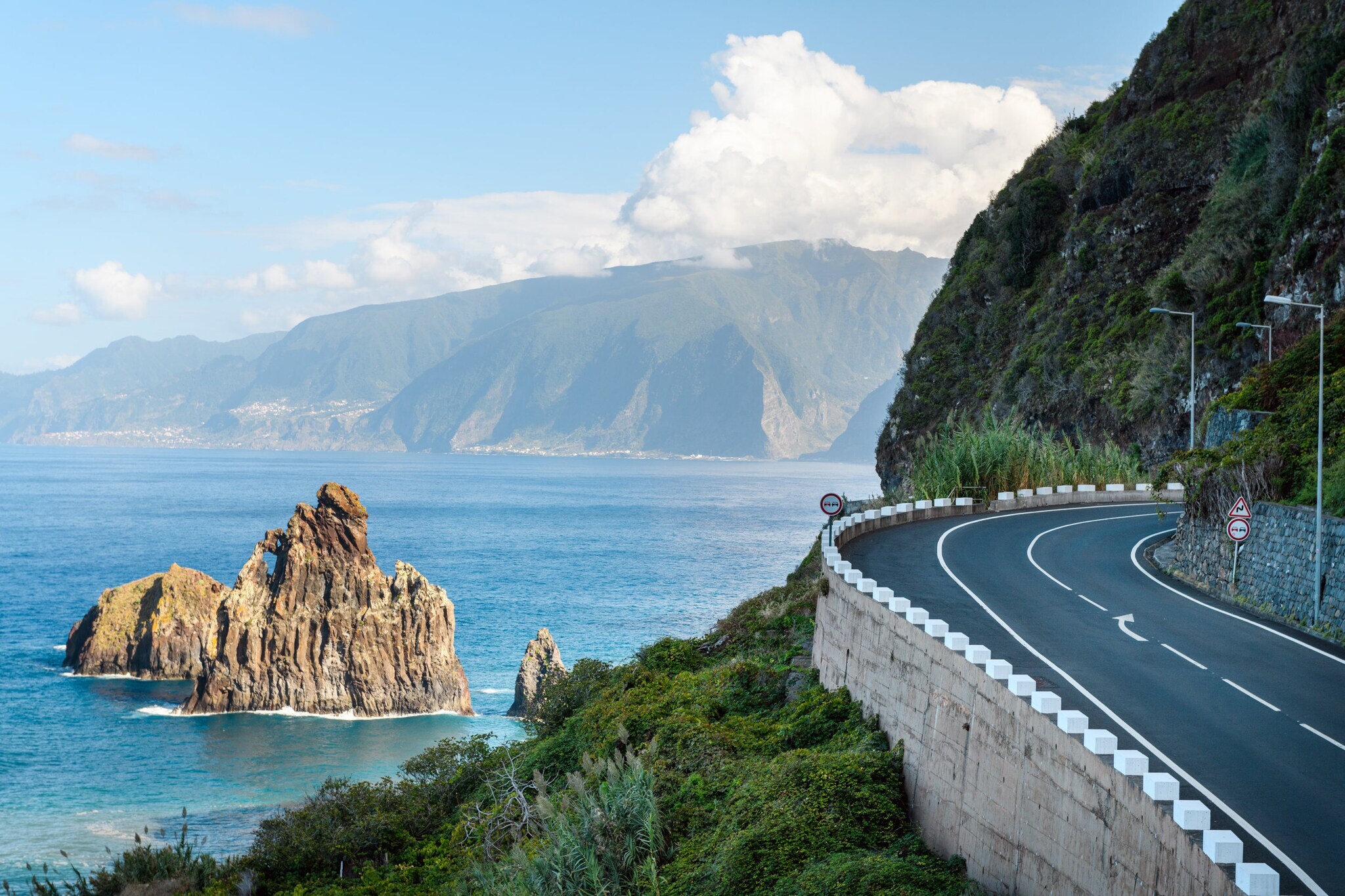 Küstenstraße am blauen Meer, im Hintergrund Berge.