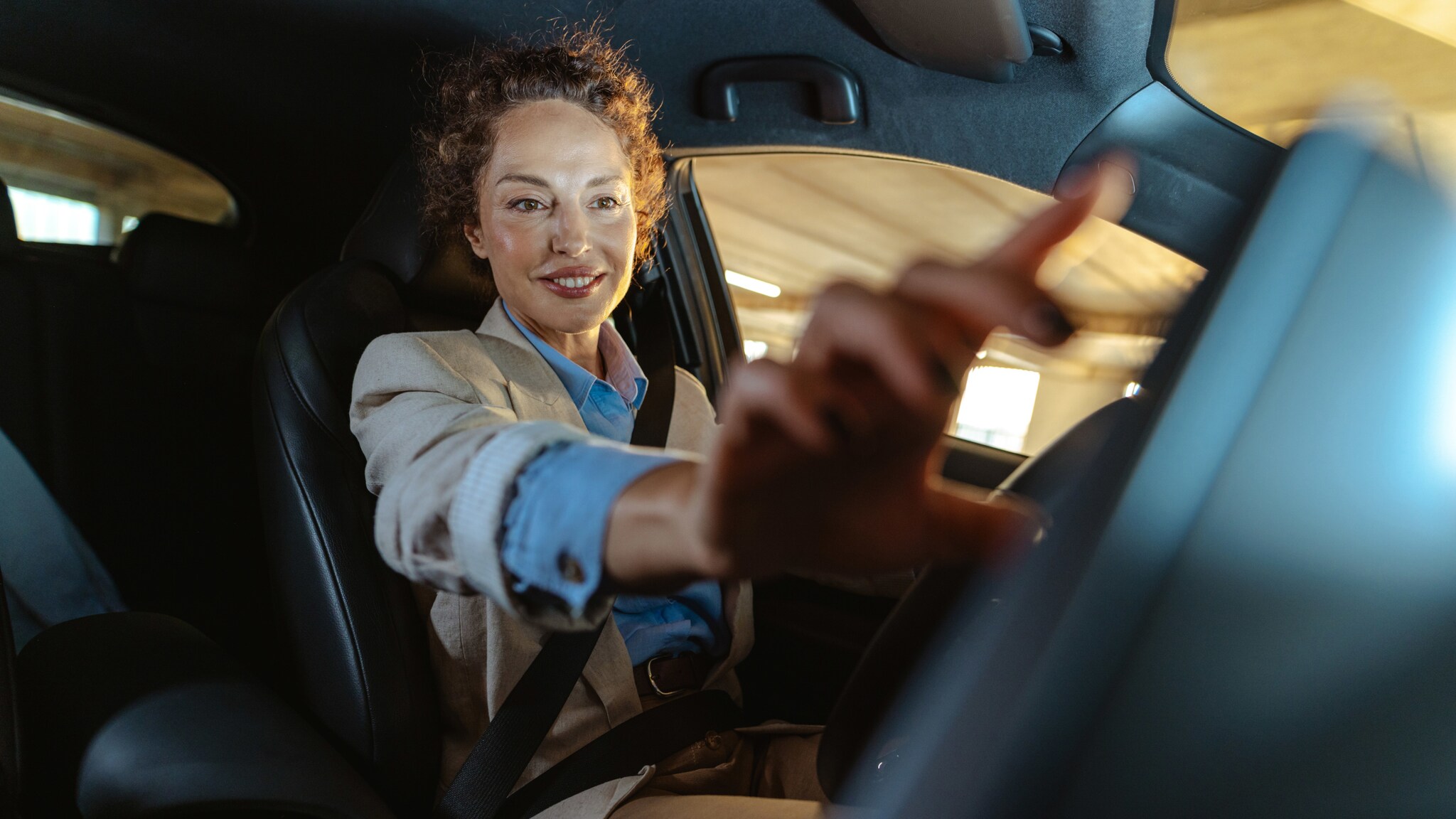Eine lächelnde Frau sitzt am Steuer eines Autos und streckt ihre Hand nach dem Armaturenbrett aus. Eine lächelnde Frau sitzt am Steuer eines Autos und streckt ihre Hand nach dem Armaturenbrett aus.