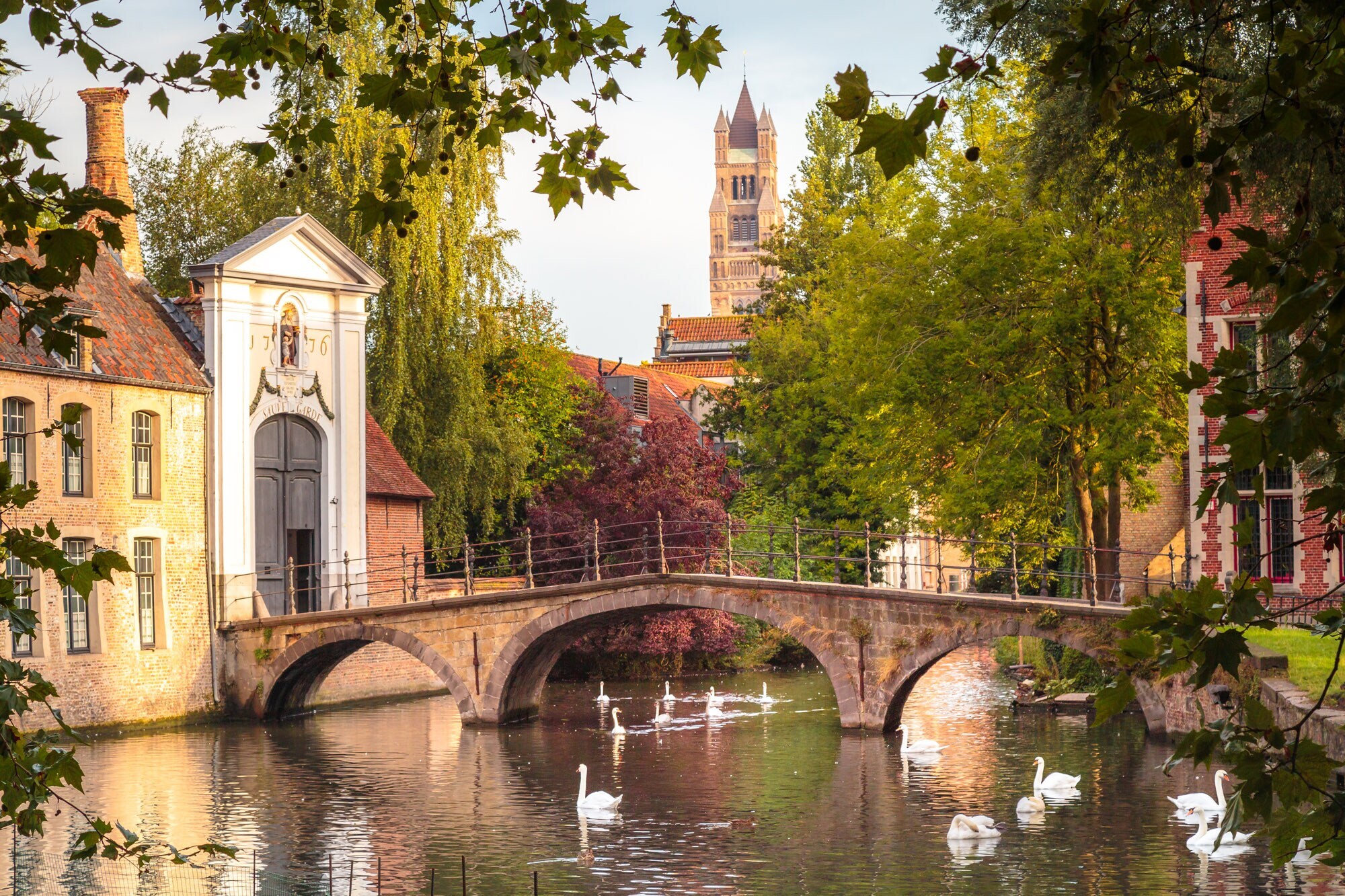 Eine mittelalterliche Stadtbrücke führt über eine Gracht mit Schwänen zum Eingang eines Klosters.