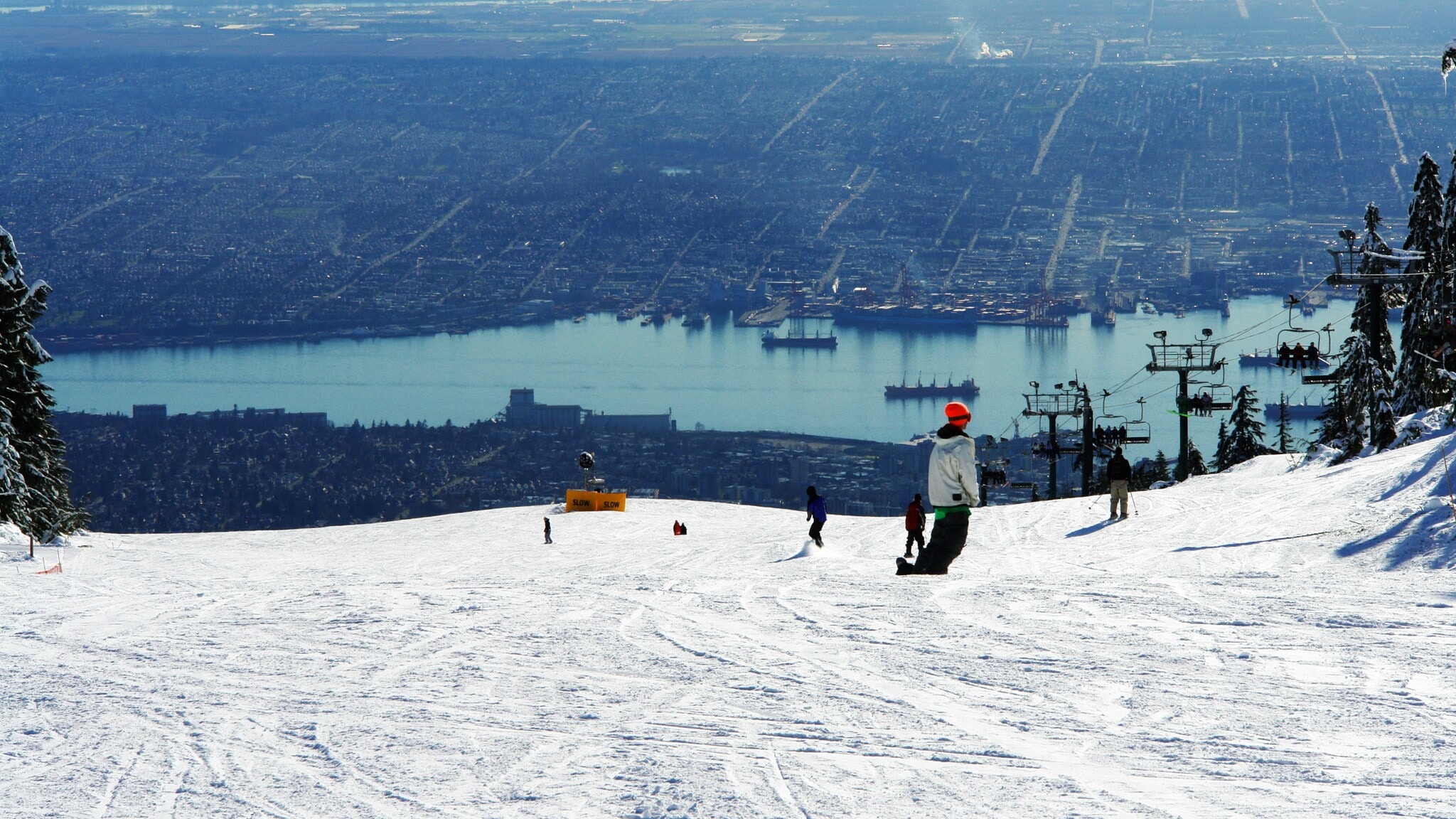 Personen auf einer Skipiste mit Sessellift und Panoramablick auf die Stadt Vancouver mit Hafen. Personen auf einer Skipiste mit Sessellift und Panoramablick auf die Stadt Vancouver mit Hafen.