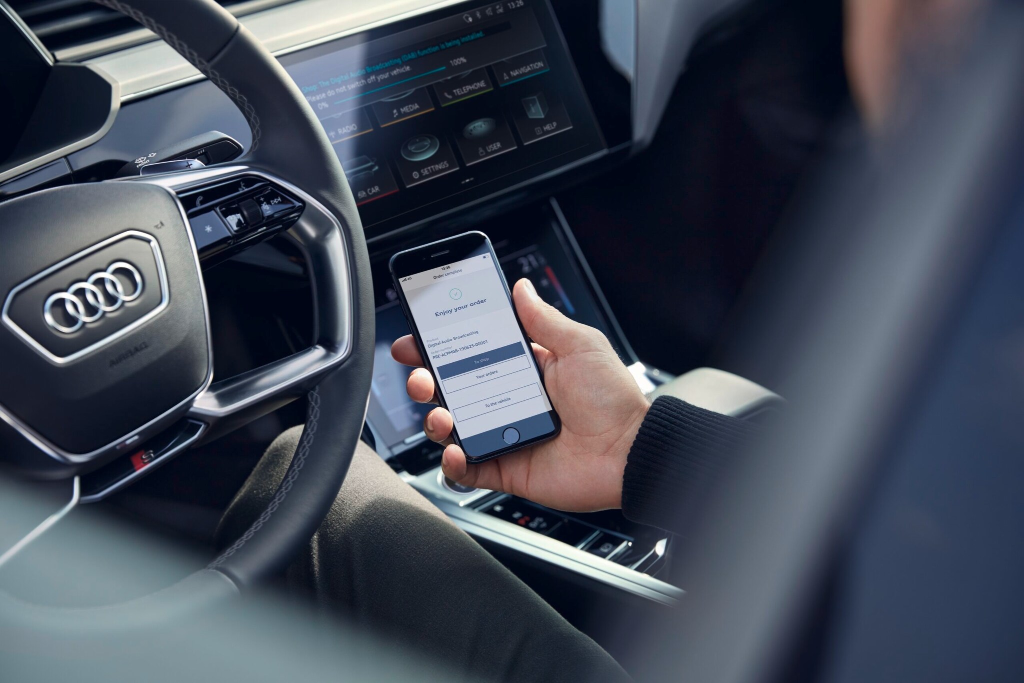 Fahrer hält im Cockpit eines Audis ein Smartphone in der Hand, um eine Funktion für das Auto zu buchen Fahrer hält im Cockpit eines Audis ein Smartphone in der Hand, um eine Funktion für das Auto zu buchen