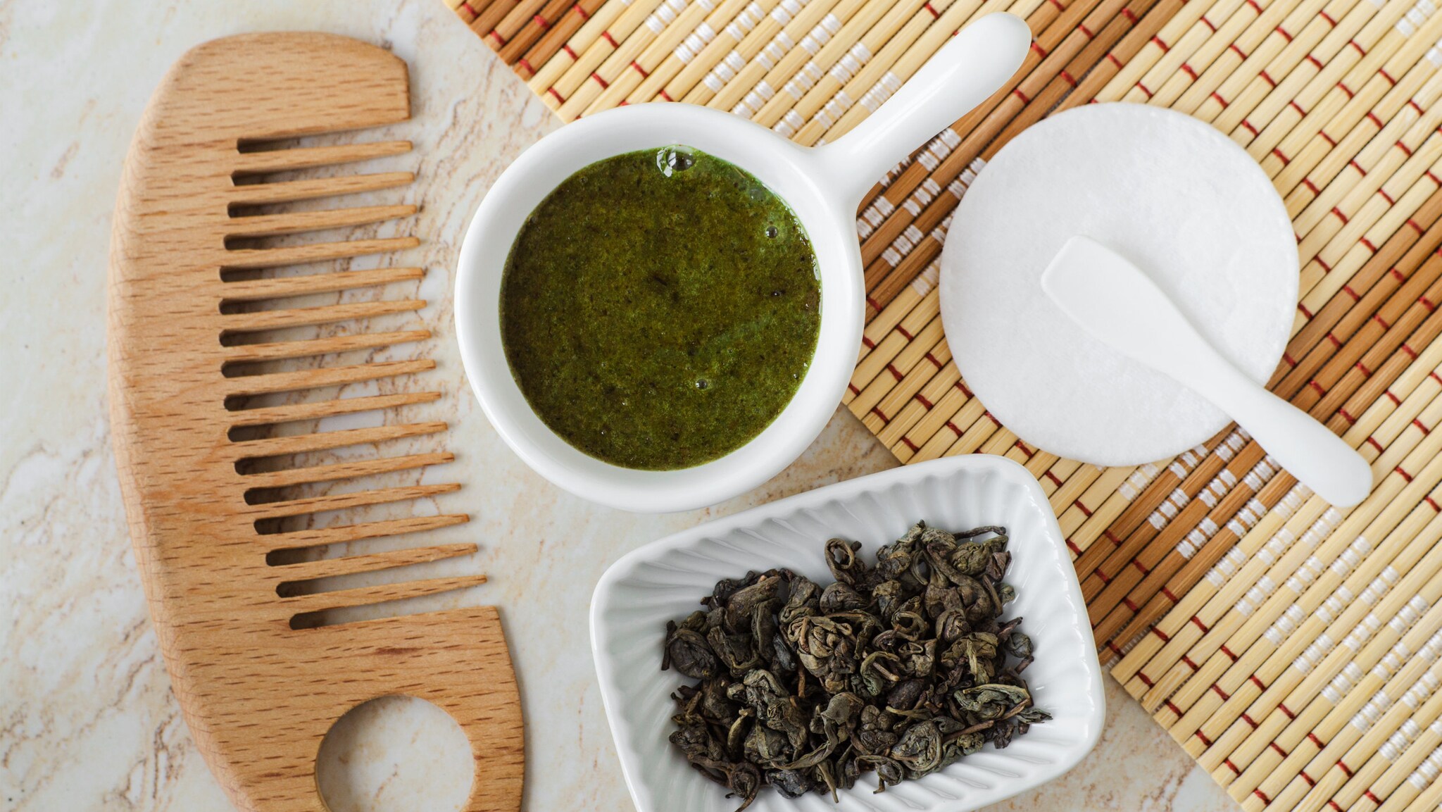 Eine Schüssel mit getrocknetem Tee, ein Gefäß mit Matcha-Peeling, ein Kamm und ein Teller mit Löffel befinden sich auf einem Tisch.