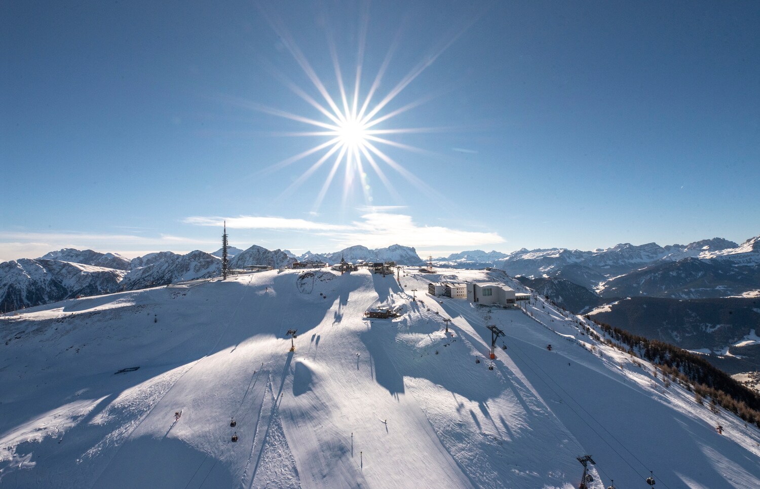 Panoramaaufnahme eines Skigebiets auf einem Gipfel mit Rundumblick über die schneebedeckte Berglandschaften bei Sonnenschein