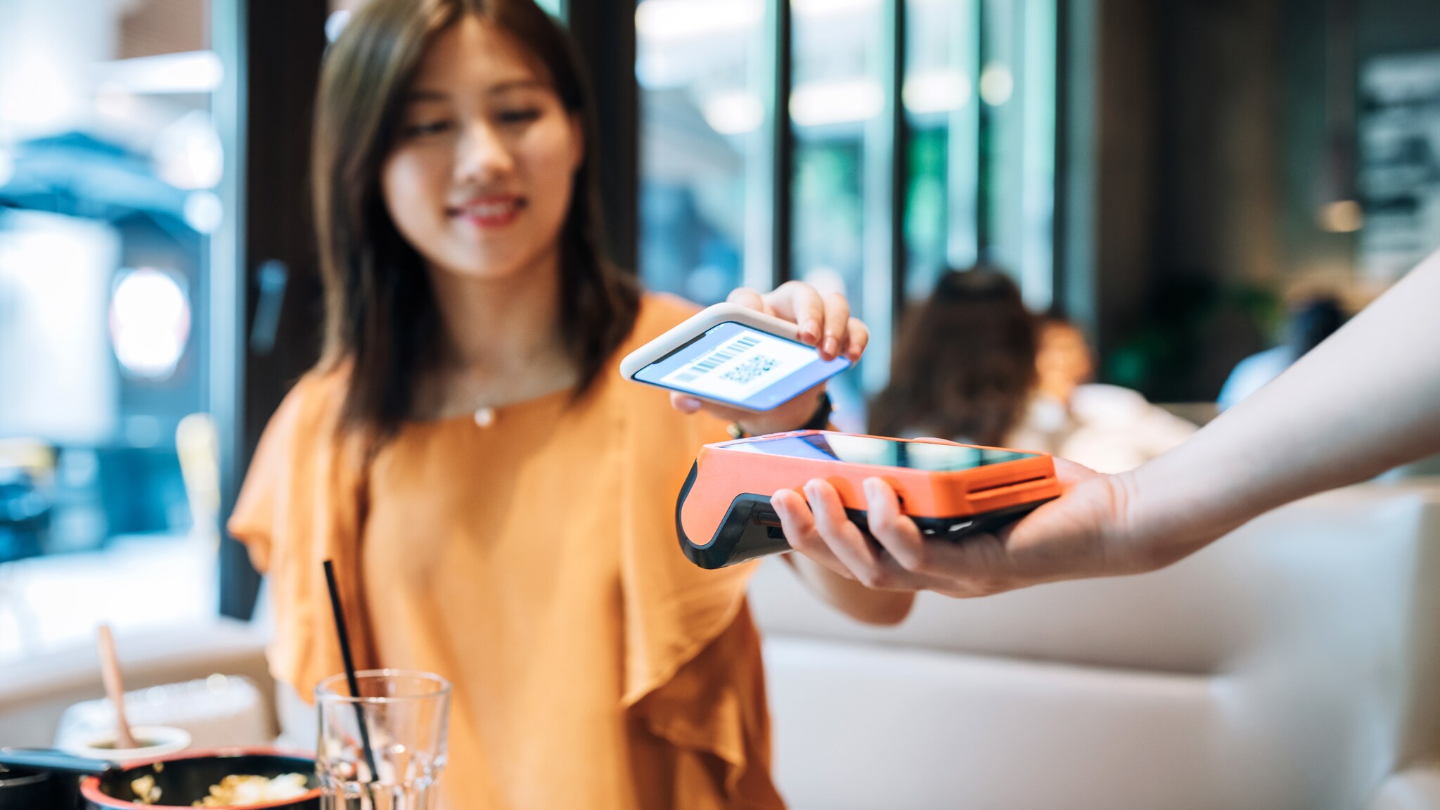 Eine Frau bezahlt mit ihrem Smartphone per App an einem Kartenlesegerät in einem Restaurant.