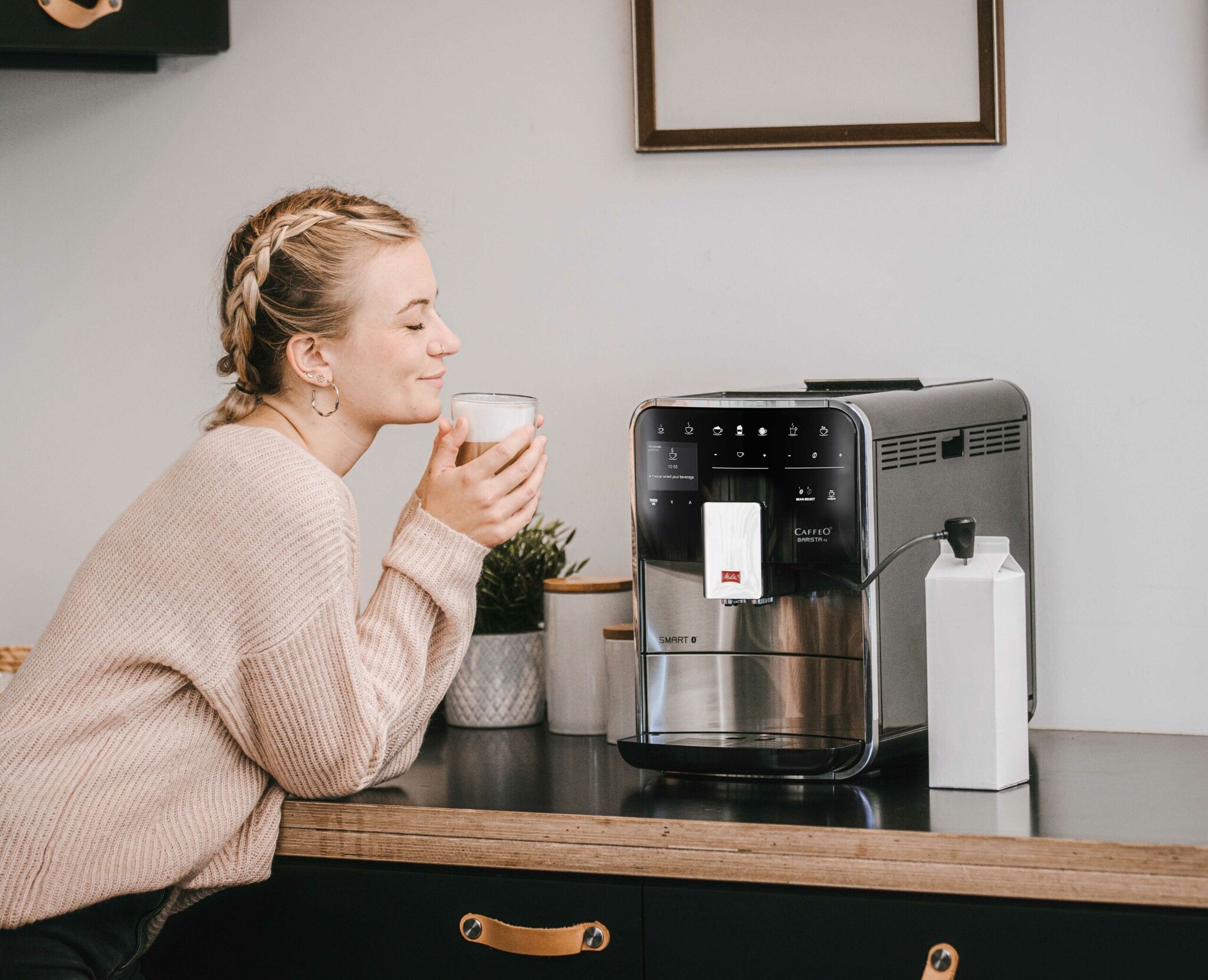 Eine Frau sitzt vor einer Kaffeemaschine und genießt ihren Kaffee Eine Frau sitzt vor einer Kaffeemaschine und genießt ihren Kaffee