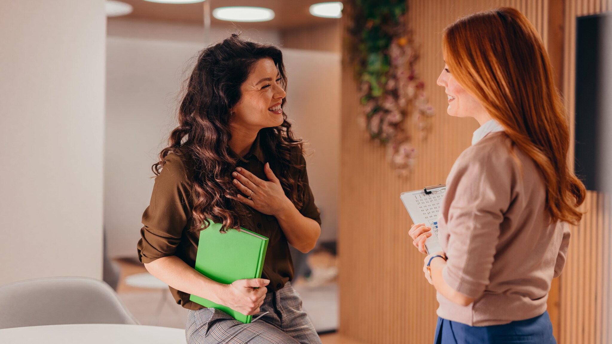 Zwei lächelnde Frauen während einer herzlichen Unterhaltung in einem Konferenzraum an, eine Frau legt dabei ihre Hand aufs Herz. Zwei lächelnde Frauen während einer herzlichen Unterhaltung in einem Konferenzraum an, eine Frau legt dabei ihre Hand aufs Herz.