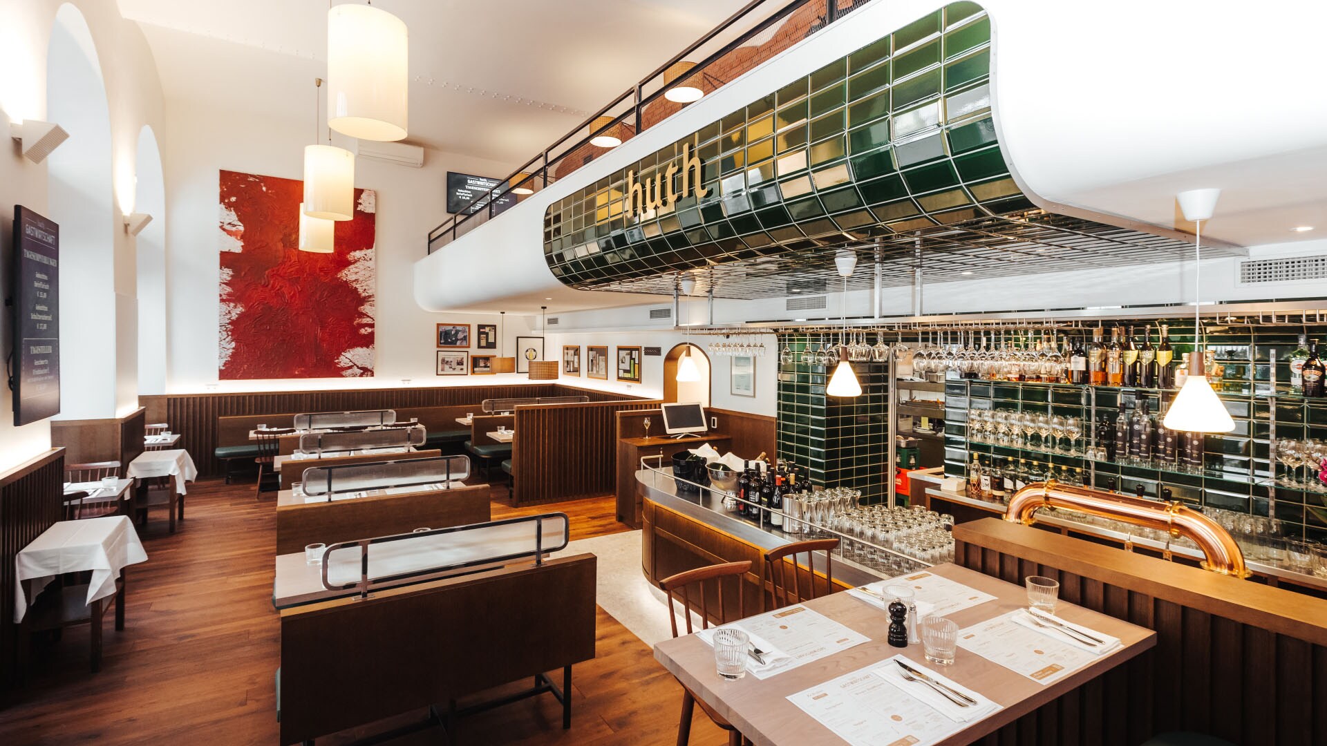Moderner Speiseraum mit Holzmobiliar und Barbereich mit grünen Kacheln mit der Aufschrift huth.