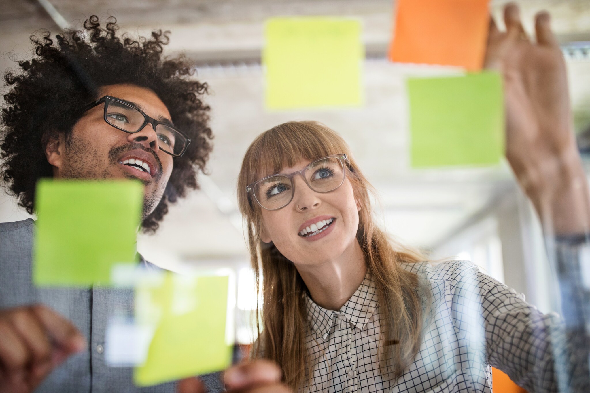 Nahaufnahme von Mann und Frau hinter einer Glasscheibe mit bunten Klebezetteln in einem Büro.