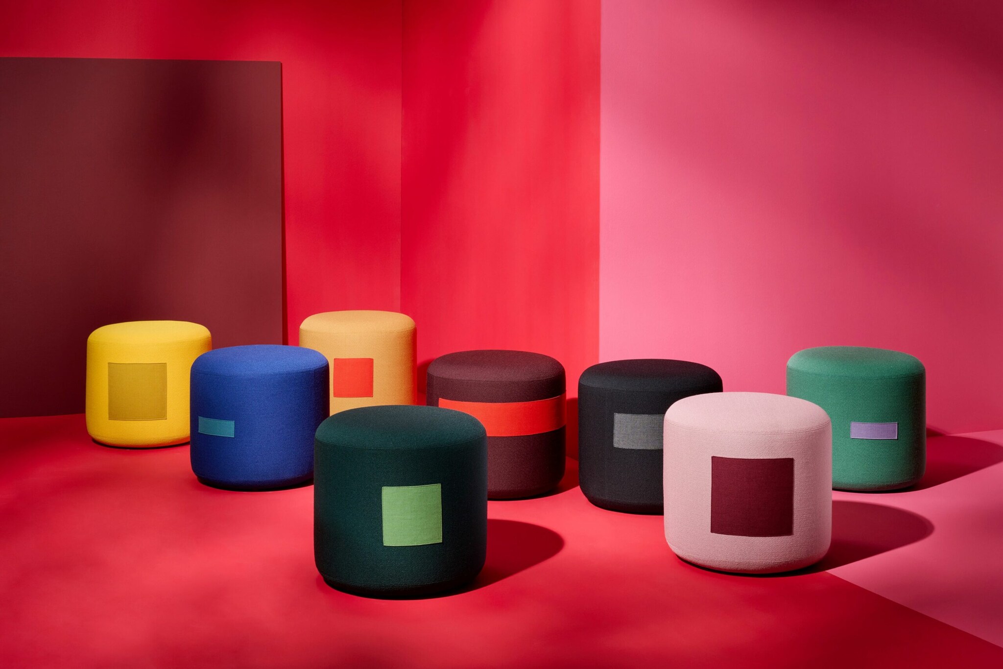 Sitzhocker von Schönbuch in verschiedenen Farben vor pink-rotem Hintergrund.