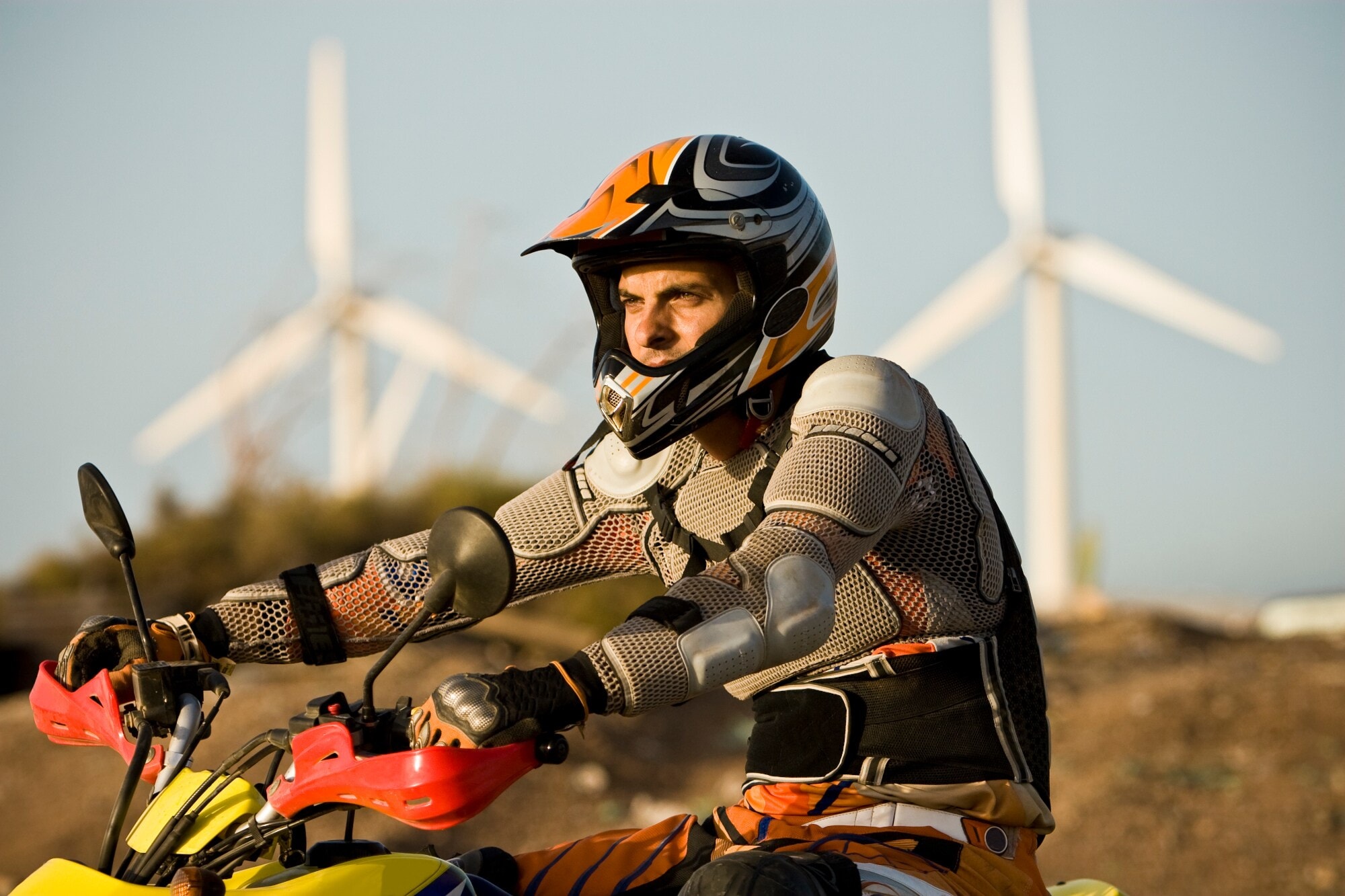 Ein Mann in Motocrosskleidung und mit Helm auf einem Bike, im Hintergrund Windräder Ein Mann in Motocrosskleidung und mit Helm auf einem Bike, im Hintergrund Windräder
