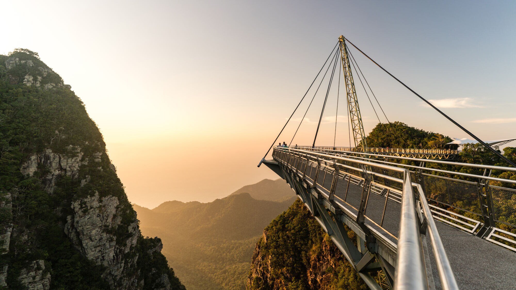 Hängende Fußgängerbrücke mit Stahlseilen über bewaldete Berge bei Sonnenuntergang auf Langkawi.