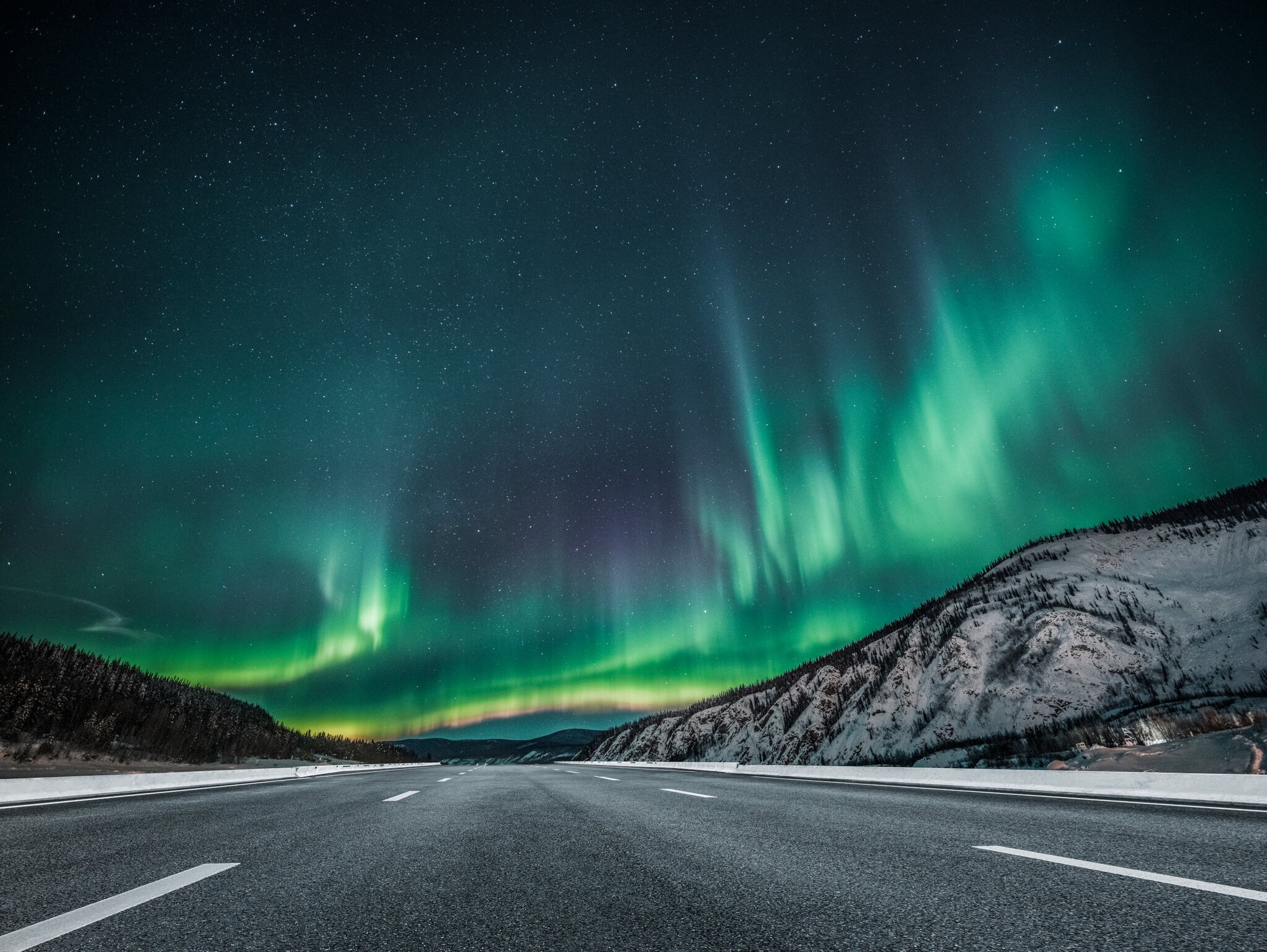 Gelb-grün schimmernde Polarlichter über einer asphaltierten Straße im Yukon.