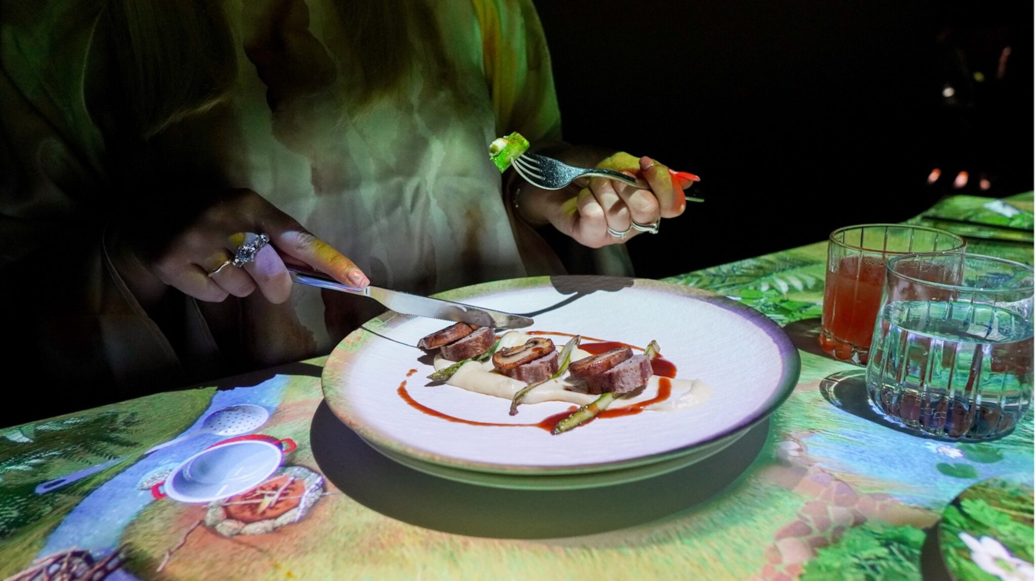 Eine Hand mit einer Gabel greift nach einem Stück Fisch auf einem Teller mit gelber Sauce und grünen Erbsen.