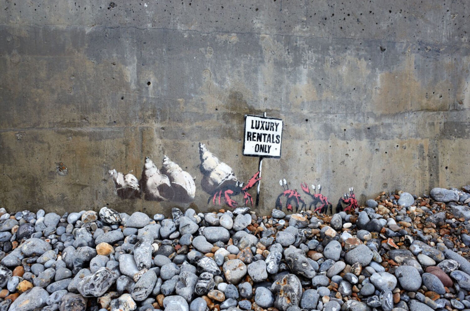 Ein Werk des Künstlers Banksy, das einen Krebs zeigt, der mehrere Schneckenmuscheln vor anderen Krebsen schützt und ein Schild mit der Aufschrift „Luxury Rentals Only“ hochhält. Ein Werk des Künstlers Banksy, das einen Krebs zeigt, der mehrere Schneckenmuscheln vor anderen Krebsen schützt und ein Schild mit der Aufschrift „Luxury Rentals Only“ hochhält.