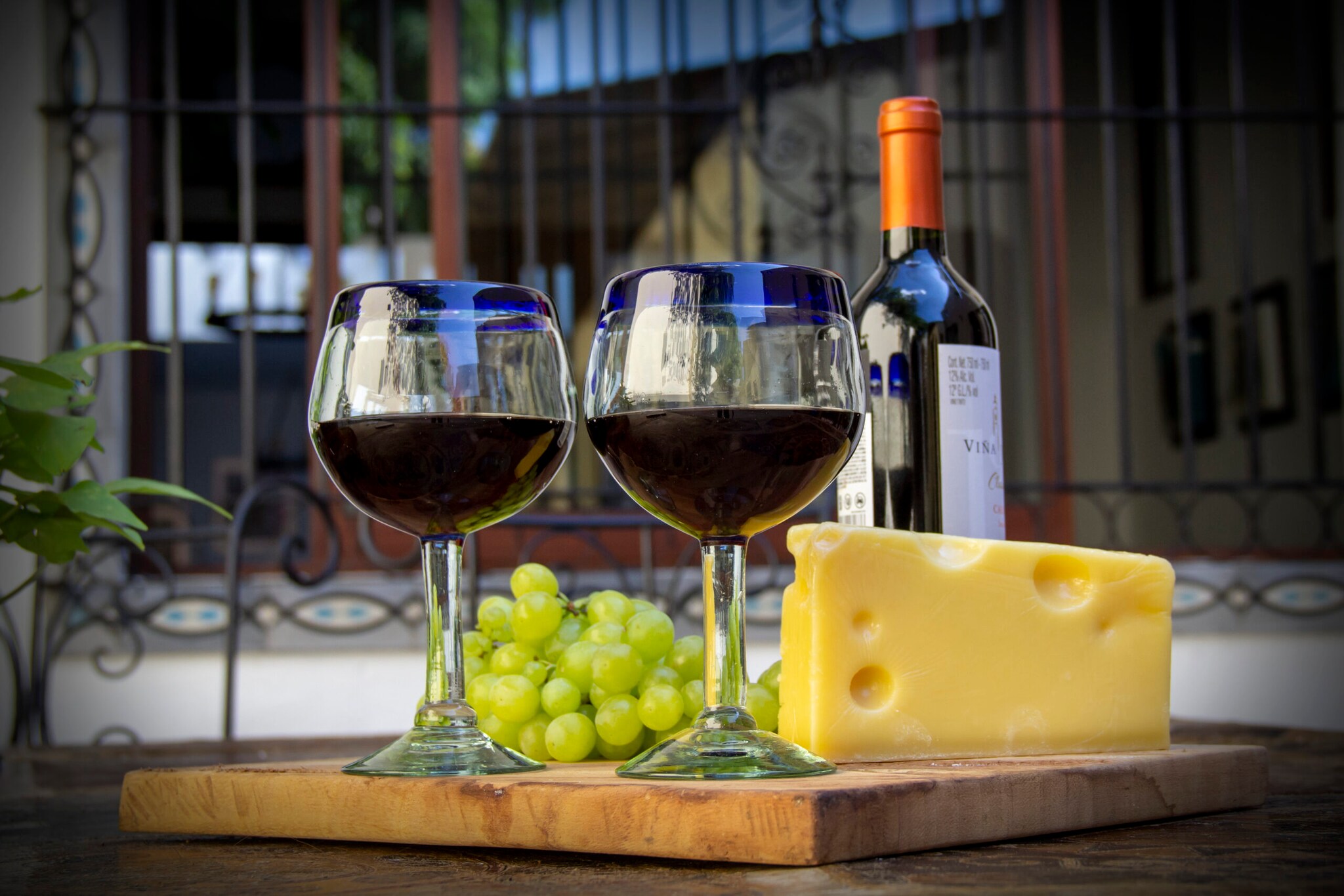 Zwei Rotweingläser sind arrangiert neben einem Stück Käse und Weintrauben