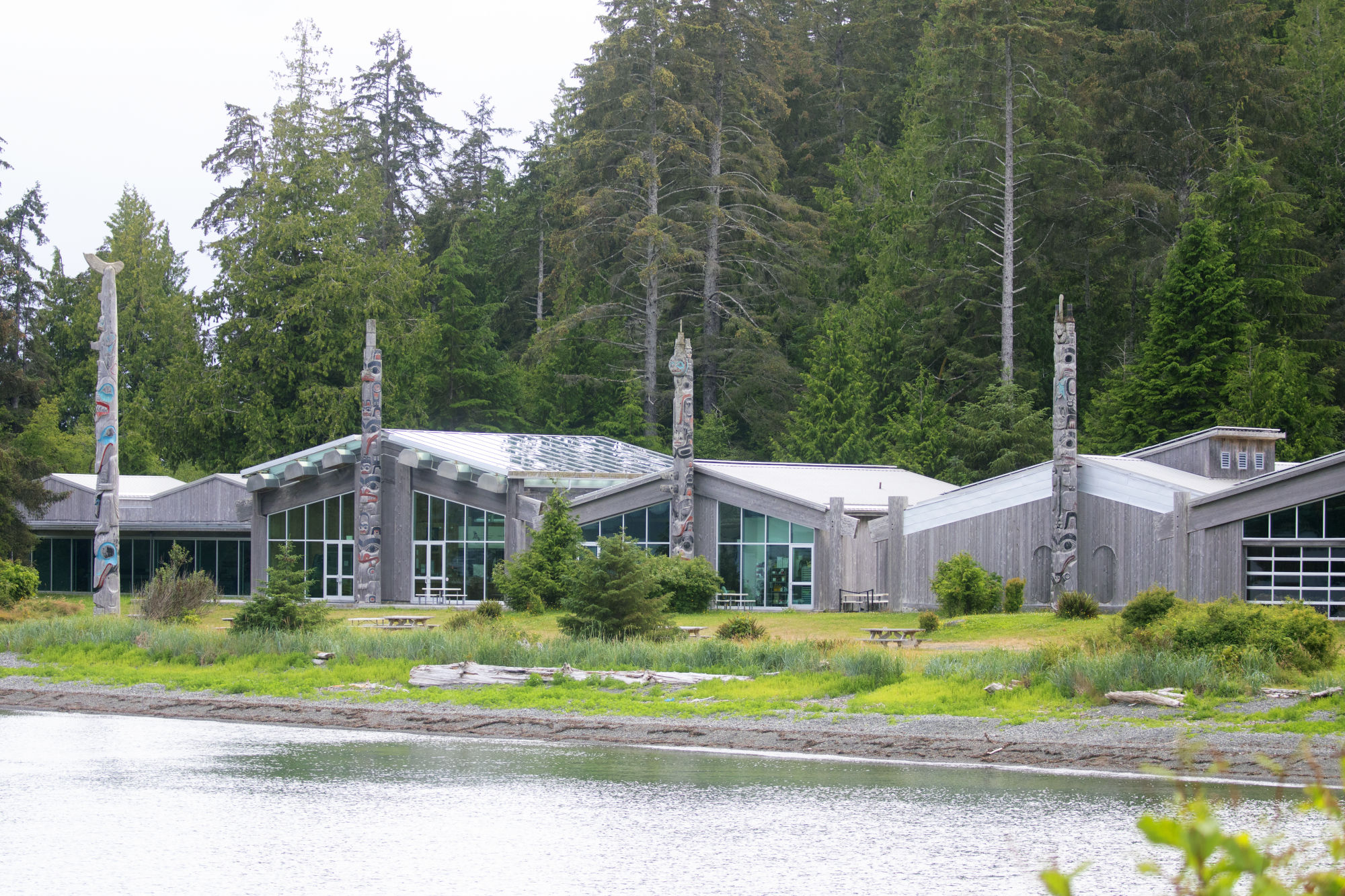 Blick auf das Haida Heritage Centre in Skidegate, das führende Kulturzentrum der Haida mit modernen Holzhäusern samt Totems am Wasser.