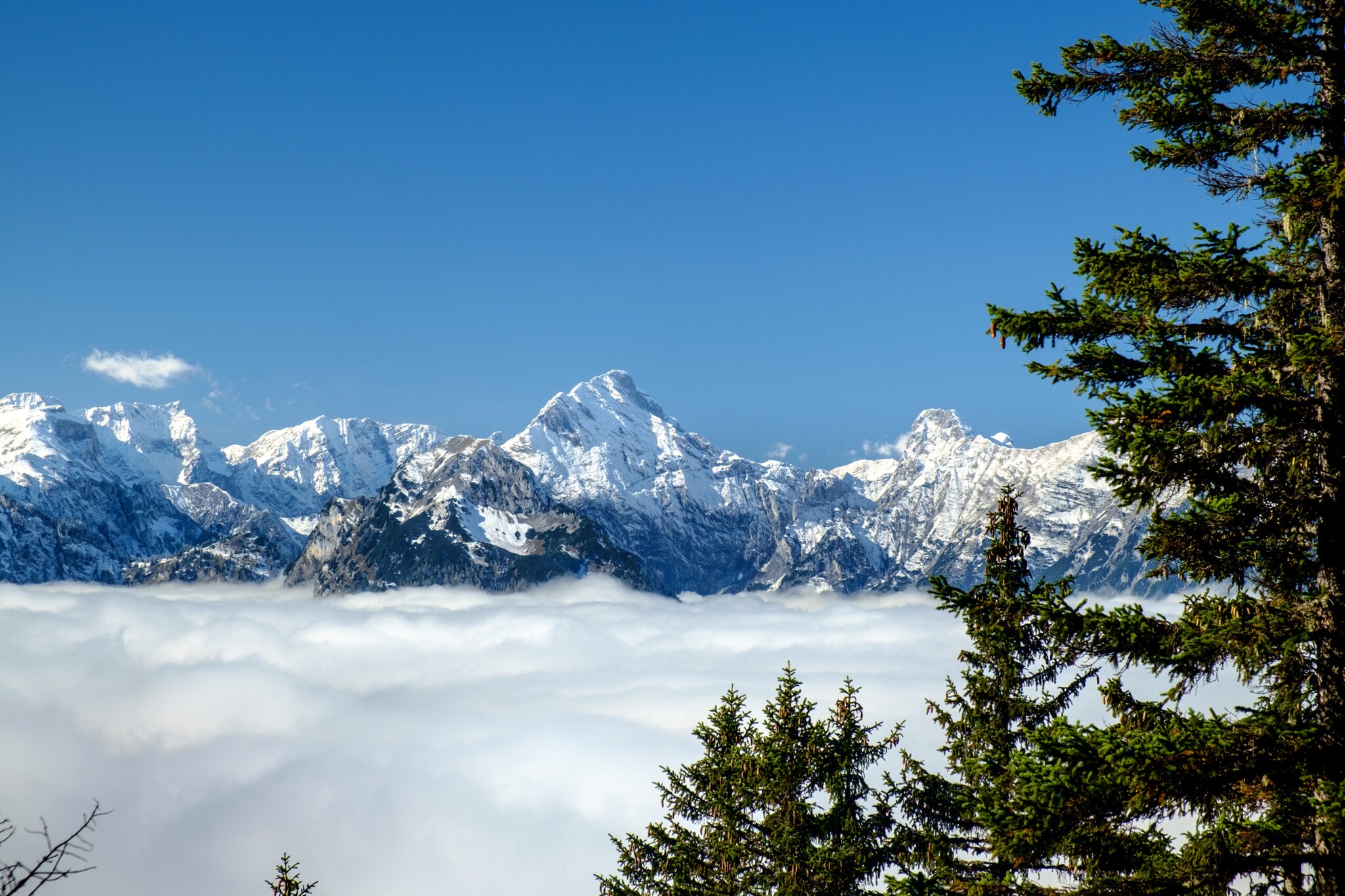 Panoramaansicht auf das Karwendelgebirge mit verschneiten Gipfeln vor strahlend blauem Himmel und dichter Wolkendecke zum Tal hin