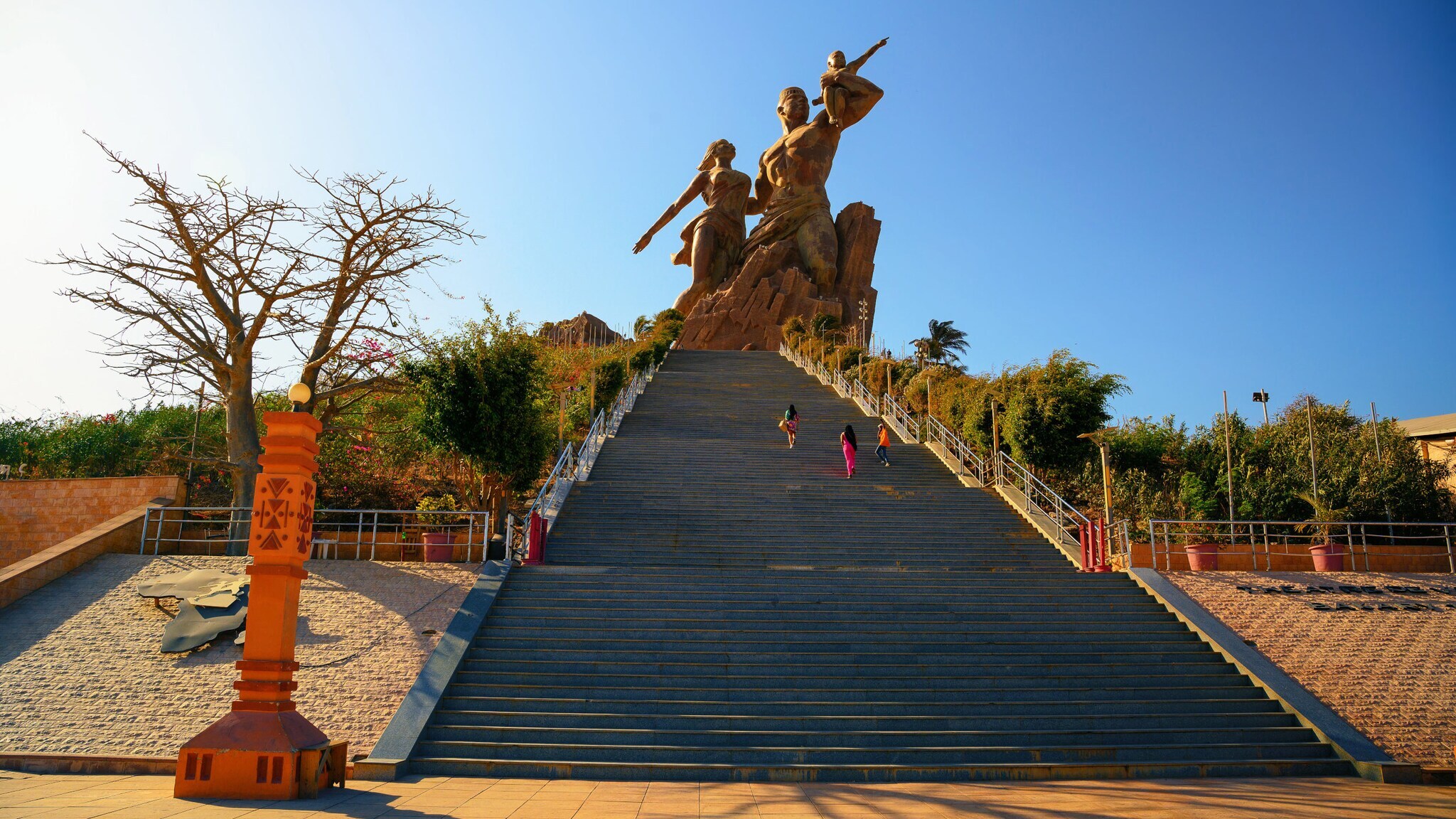 Personen auf einer pyramidenförmigen Treppe eines Denkmals mit großer Bronzestatue unter blauem Himmel. Personen auf einer pyramidenförmigen Treppe eines Denkmals mit großer Bronzestatue unter blauem Himmel.