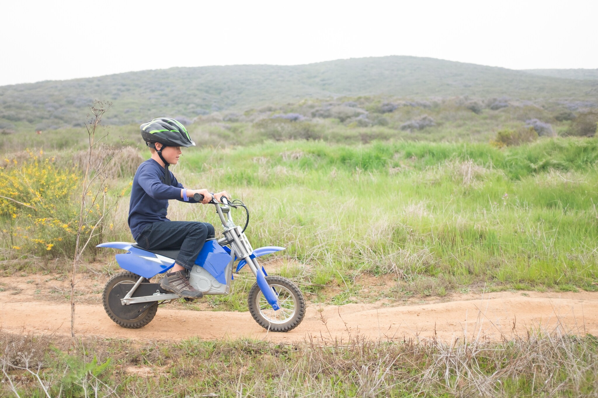 Ein Junge fährt ein Elektro-Kindermotorrad auf einem Feldweg.