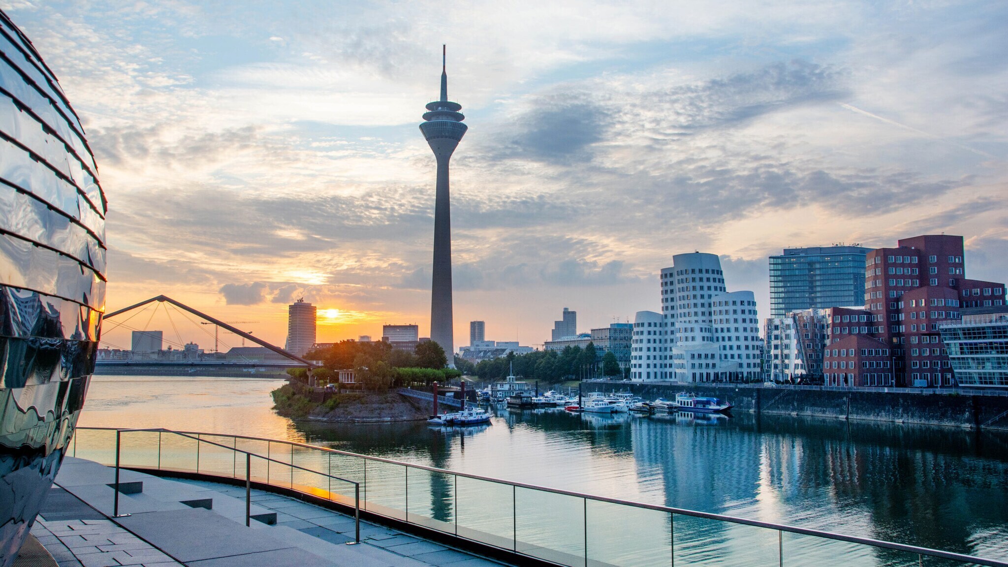 Blick auf den Rheinturm und die MedienHafen-Gebäude in Düsseldorf bei Sonnenuntergang mit Hafenbecken im Vordergrund Blick auf den Rheinturm und die MedienHafen-Gebäude in Düsseldorf bei Sonnenuntergang mit Hafenbecken im Vordergrund