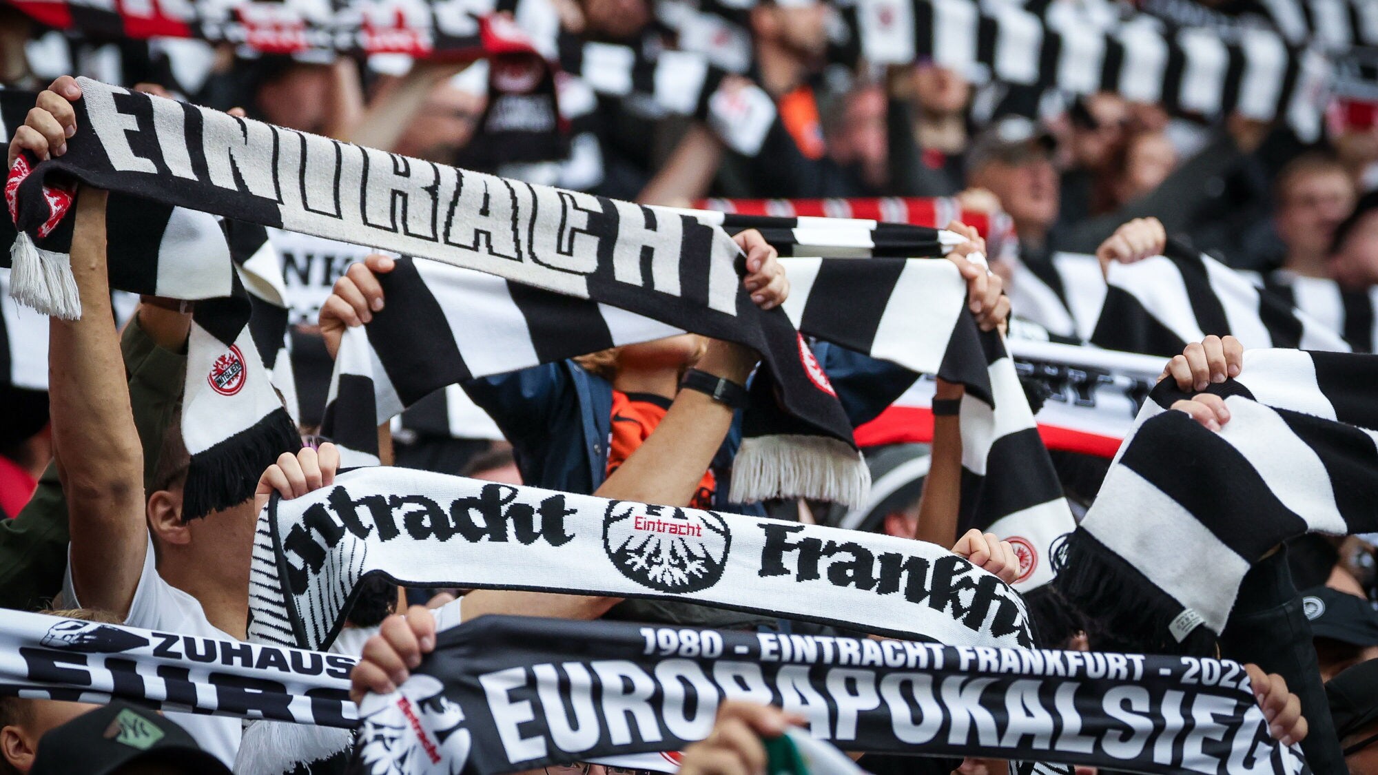 Zahlreiche hochgehaltene schwarz-weiße Schals mit „Eintracht Frankfurt“ Aufdruck in den Händen von Personen auf einer Tribüne.