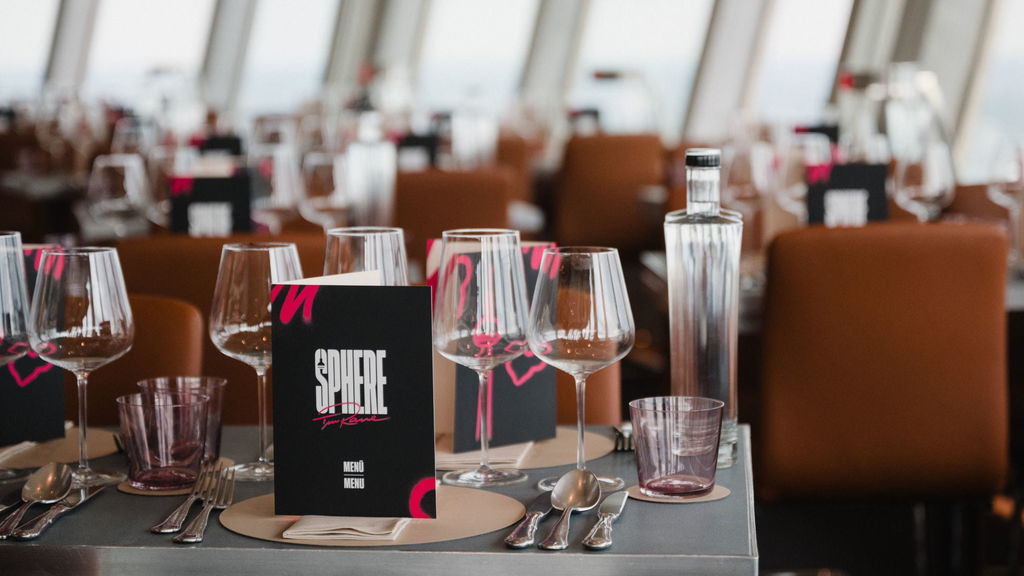 Tischgedeck in einem Restaurant mit Gläsern, einer Flasche und einer Speisekarte mit dem Titel 'SPHERE'. Im Hintergrund sind weitere Tische sichtbar. Tischgedeck in einem Restaurant mit Gläsern, einer Flasche und einer Speisekarte mit dem Titel 'SPHERE'. Im Hintergrund sind weitere Tische sichtbar.