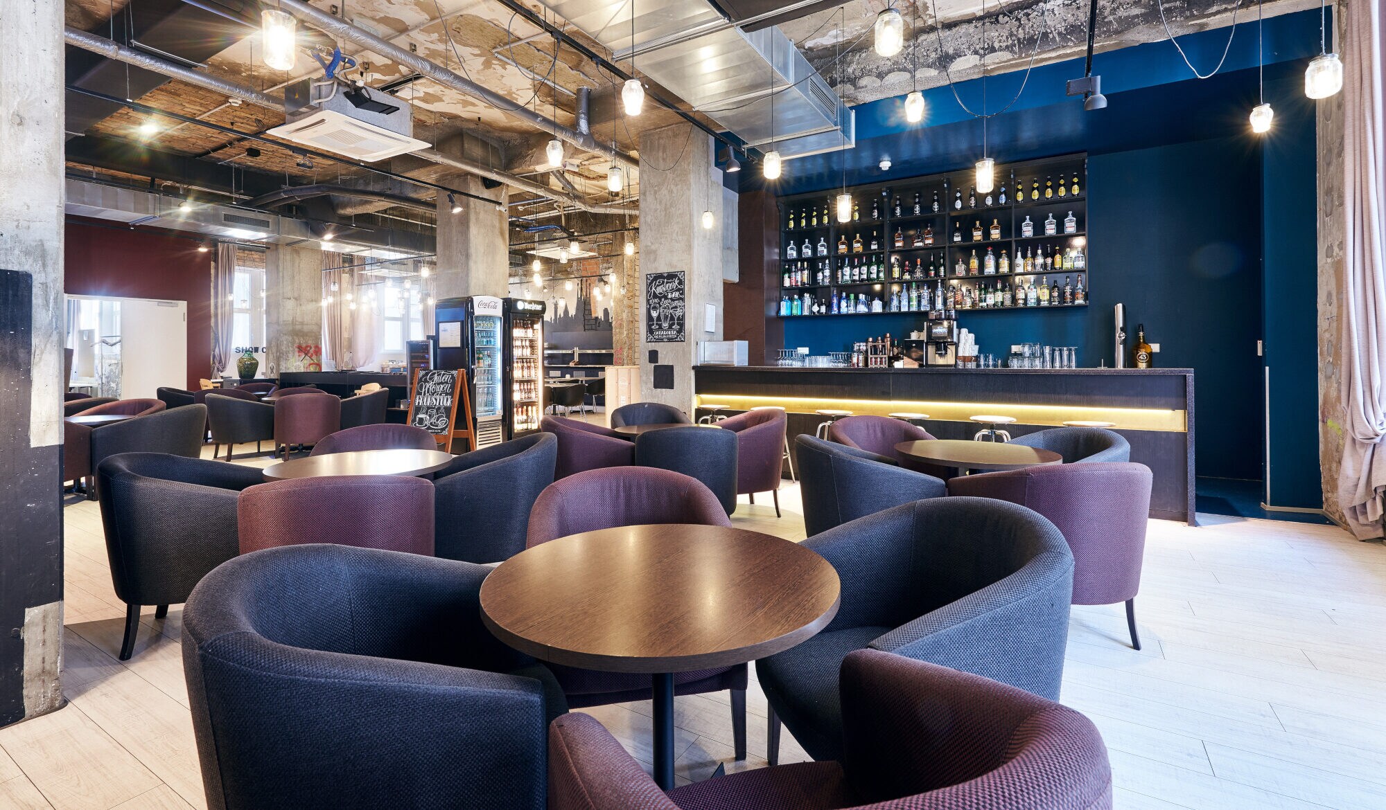 Eine Hotellobby mit Sitzgelegenheiten vor einer Bar unter einer offenen Raumdecke im Industriestil.