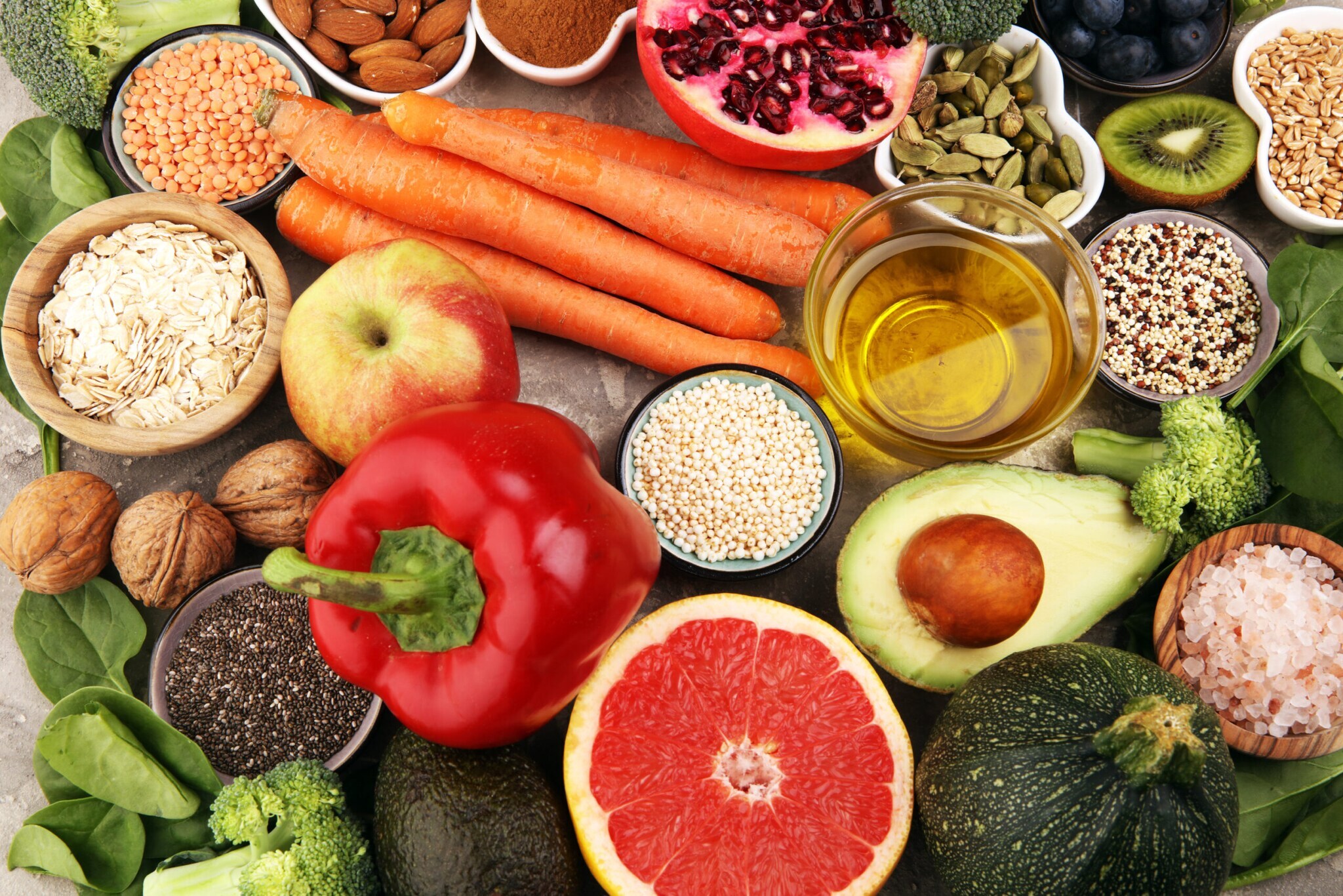 Aufsicht unterschiedlicher Obst- und Gemüsesorten neben kleinen Schalen mit Körnern, Hülsenfrüchten und Öl