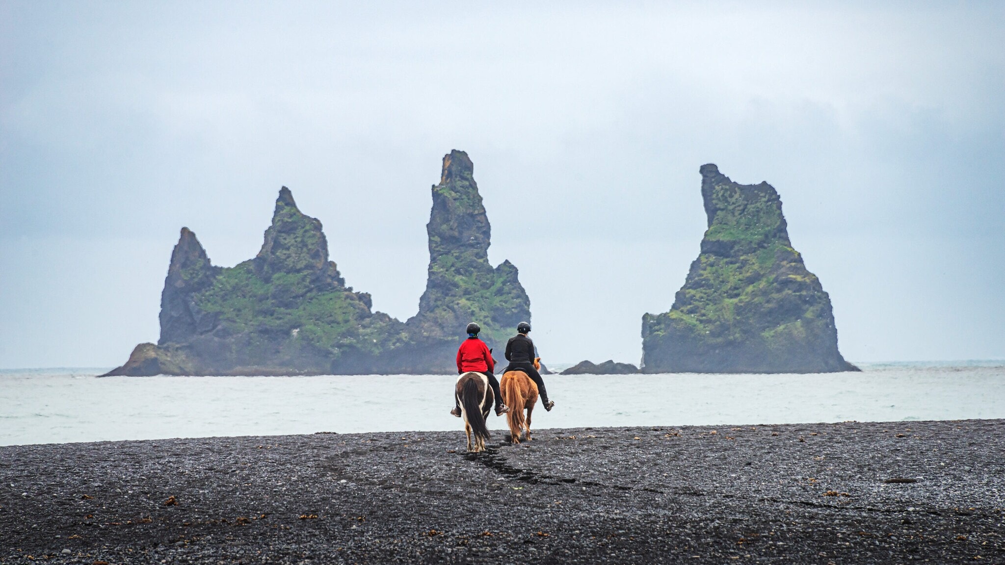 Zwei Menschen auf Pferden vor den Lavasäulen nahe Vík in Südisland Zwei Menschen auf Pferden vor den Lavasäulen nahe Vík in Südisland