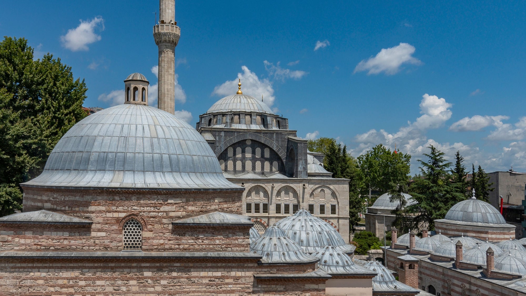 Dach eines türkischen Bads mit unterschiedlichen Kuppeln vor einer Moschee unter blauem Himmel. Dach eines türkischen Bads mit unterschiedlichen Kuppeln vor einer Moschee unter blauem Himmel.