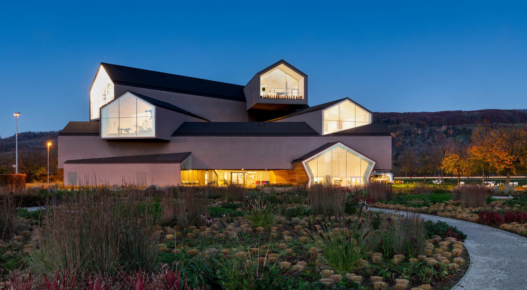 Ein geometrisches Bauwerk in der Dämmerung, die Glasfronten sind von innen erleuchtet.