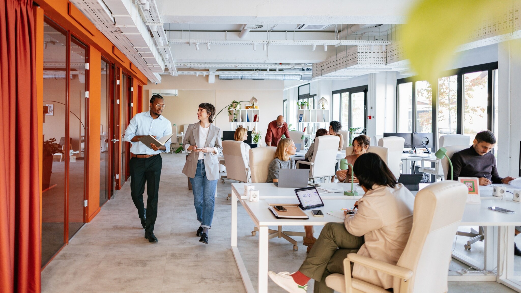 Mehrere Personen stehen oder sitzen an Arbeitsplätzen in einem modernen Großraumbüro. Mehrere Personen stehen oder sitzen an Arbeitsplätzen in einem modernen Großraumbüro.
