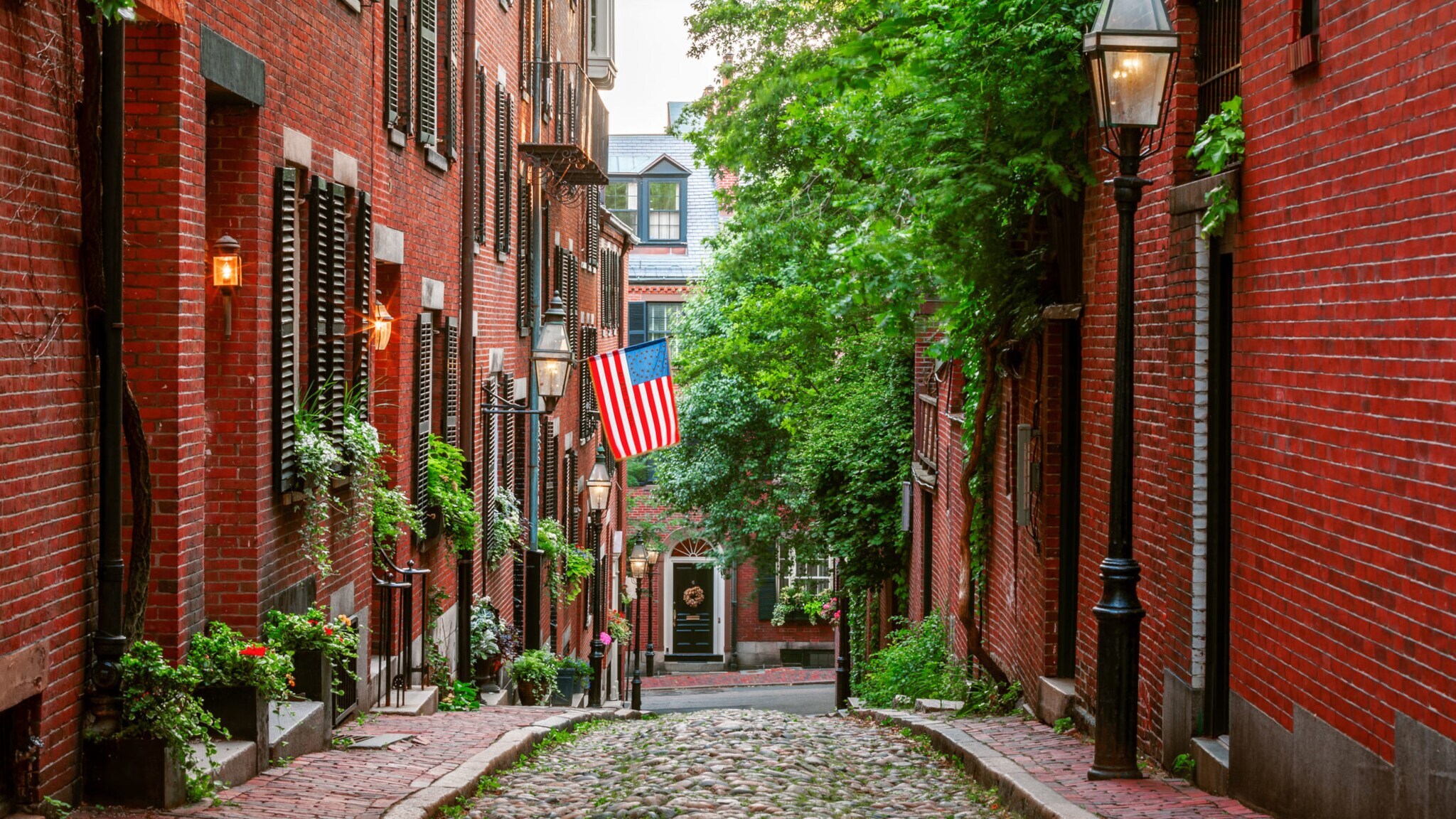 Acorn Street in Boston mit Kopfsteinpflaster und Laternen, an einer Hauswand hängt eine USA-Flagge.