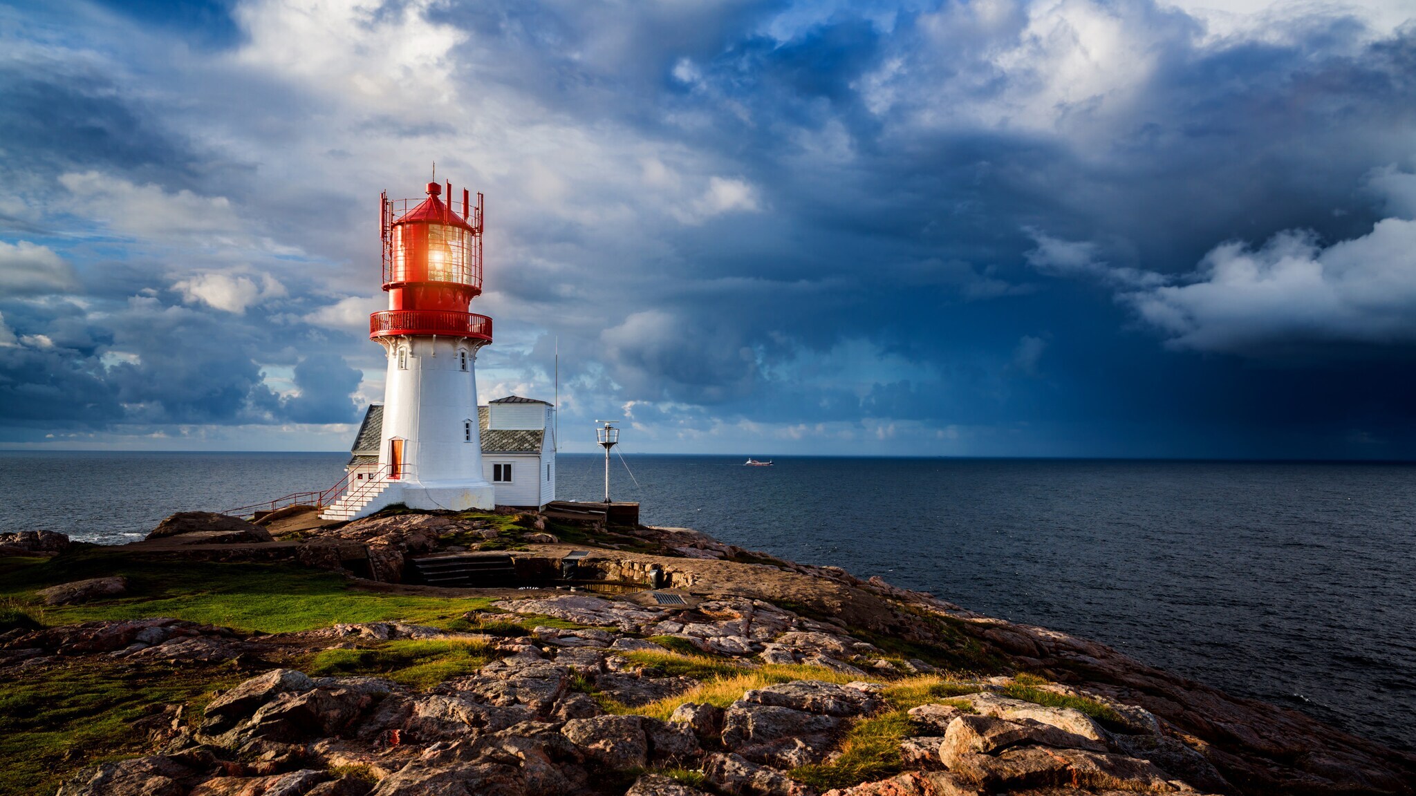 Roter und weißer Leuchtturm auf felsiger Küste unter dramatischem bewölktem Himmel am Meer in Norwegen. Roter und weißer Leuchtturm auf felsiger Küste unter dramatischem bewölktem Himmel am Meer in Norwegen.