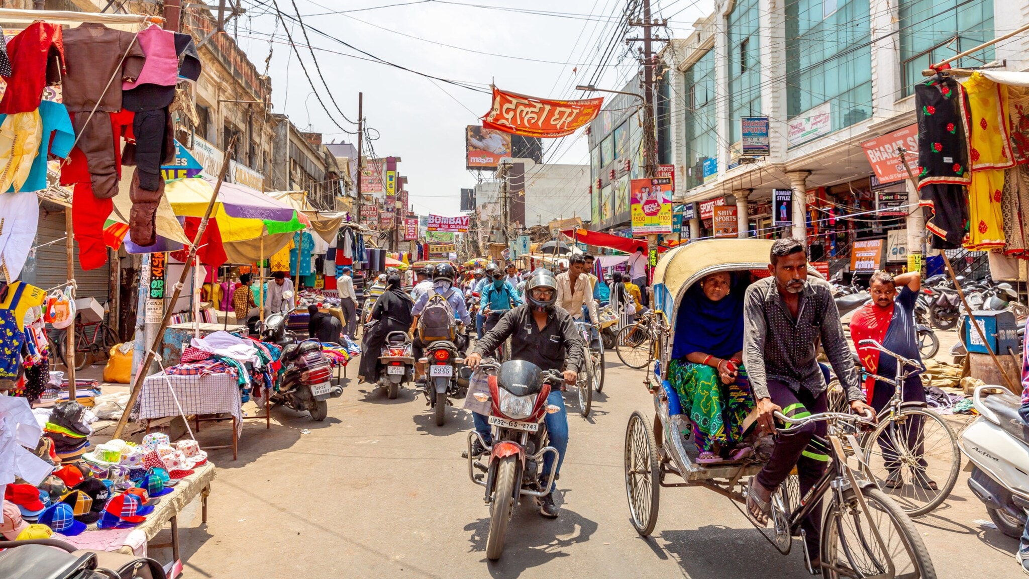 Belebte Straßenmarkt-Szene mit Menschen, Motorrädern, Fahrradrikschas und bunten Ständen in Delhi Belebte Straßenmarkt-Szene mit Menschen, Motorrädern, Fahrradrikschas und bunten Ständen in Delhi