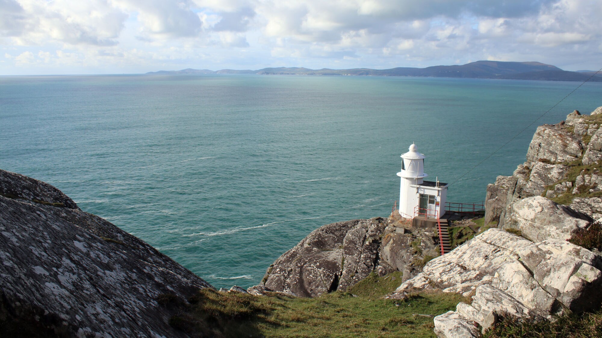 Ein weißer Leuchtturm steht auf einer Klippe über dem Meer, umgeben von Felsen und Gras. Der Himmel ist bewölkt mit einigen blauen Abschnitten. Ein weißer Leuchtturm steht auf einer Klippe über dem Meer, umgeben von Felsen und Gras. Der Himmel ist bewölkt mit einigen blauen Abschnitten.