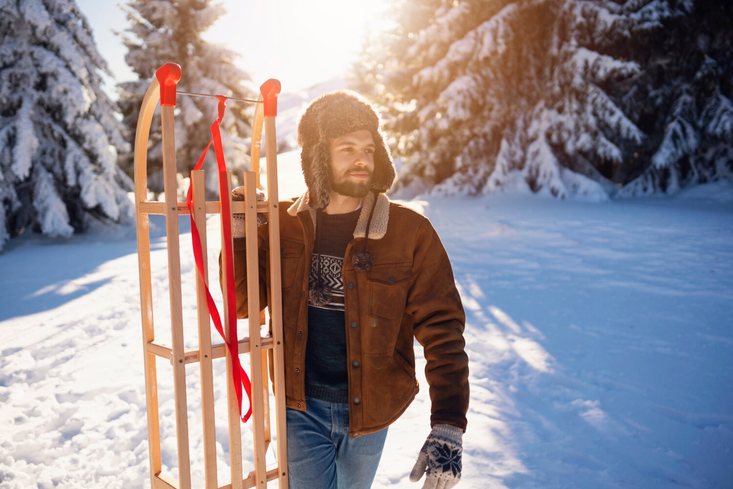 Ein Mann in Winterkleidung mit einem Schlitten in schneebedeckter Waldlandschaft.