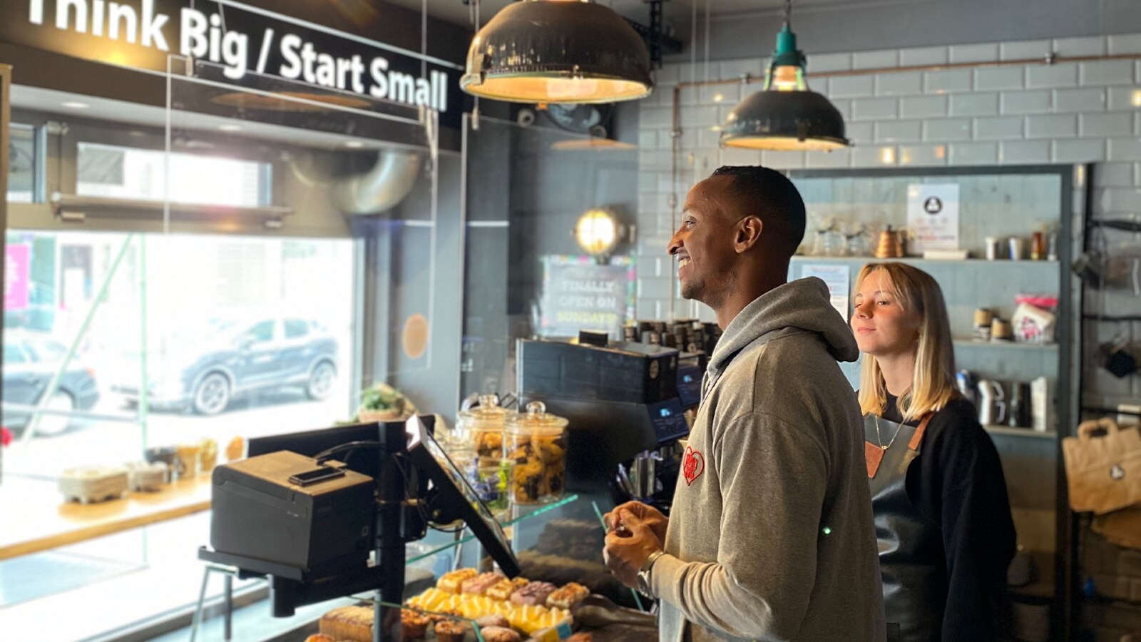 Zwei Personen stehen hinter der Verkaufstheke eines kleinen Cafés Zwei Personen stehen hinter der Verkaufstheke eines kleinen Cafés