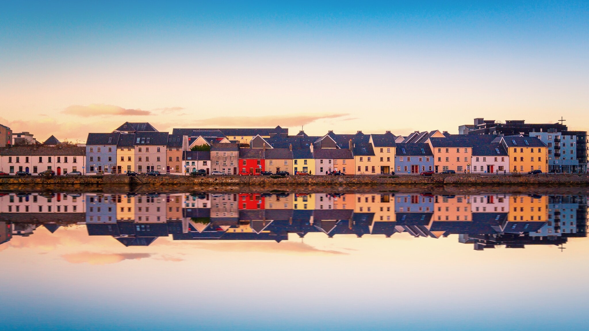 Bunte Häuser in Galway, Irland, entlang eines ruhigen Wassers mit Spiegelung. Die Gebäude sind in verschiedenen Farben, darunter Rot, Gelb und Weiß. Bunte Häuser in Galway, Irland, entlang eines ruhigen Wassers mit Spiegelung. Die Gebäude sind in verschiedenen Farben, darunter Rot, Gelb und Weiß.