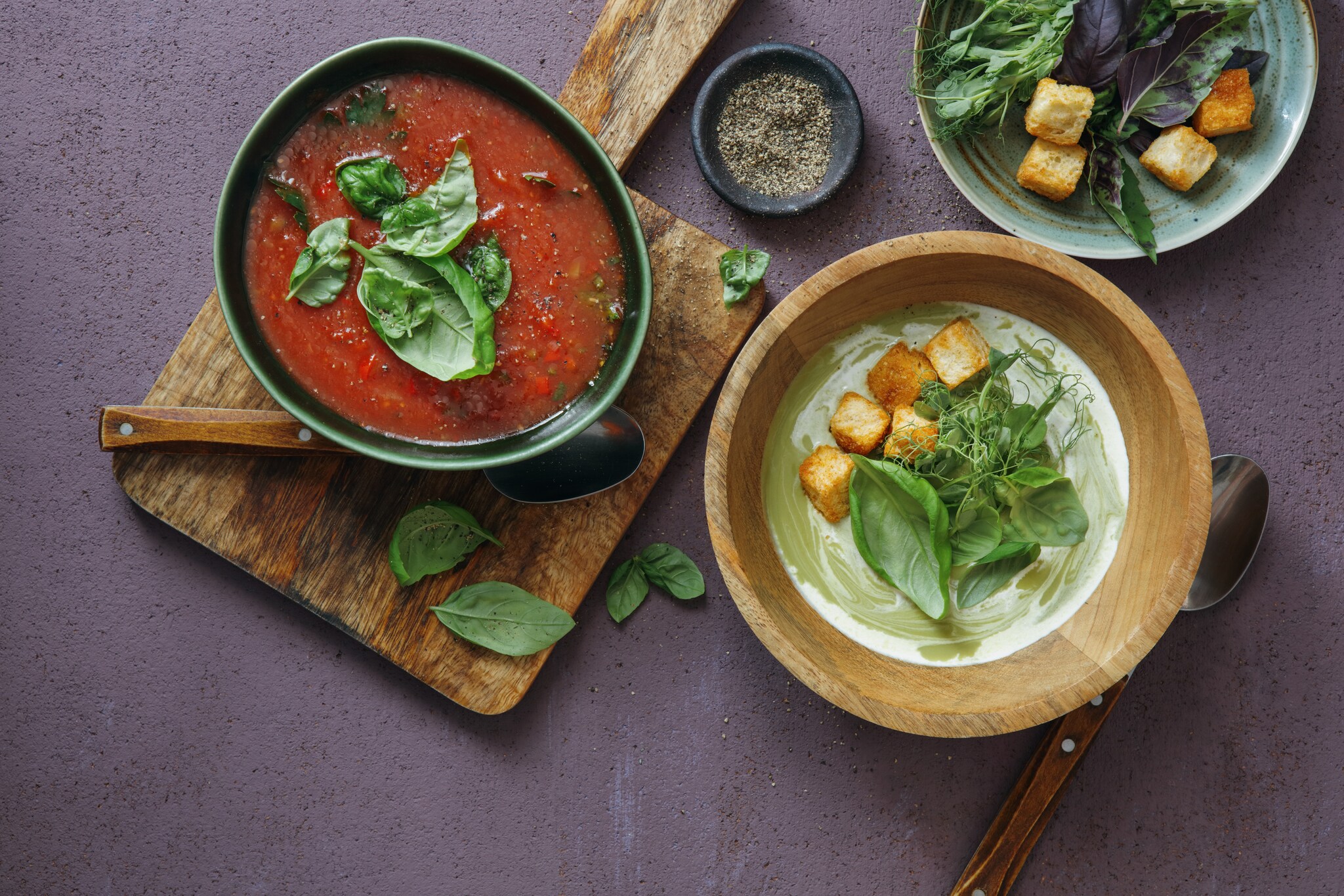 Aufsicht einer roten und einer grünen Gemüsesuppe, garniert mit Croutons und Kräutern, in Schalen auf einem Tisch Aufsicht einer roten und einer grünen Gemüsesuppe, garniert mit Croutons und Kräutern, in Schalen auf einem Tisch