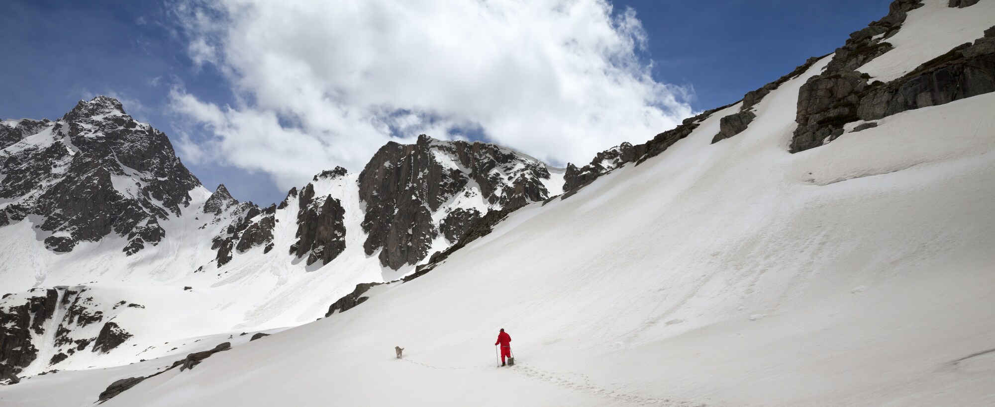 Ein Wanderer mit Hund läuft durch Tiefschnee im Gebirge Ein Wanderer mit Hund läuft durch Tiefschnee im Gebirge