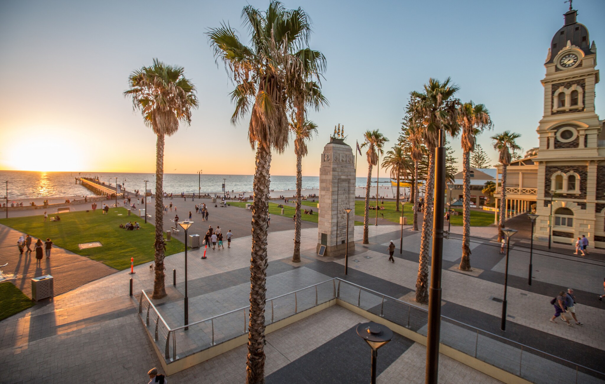 Ein Platz mit Palmen und einem Denkmal aus Stein vor dem Meer in Glenelg nahe Adelaide